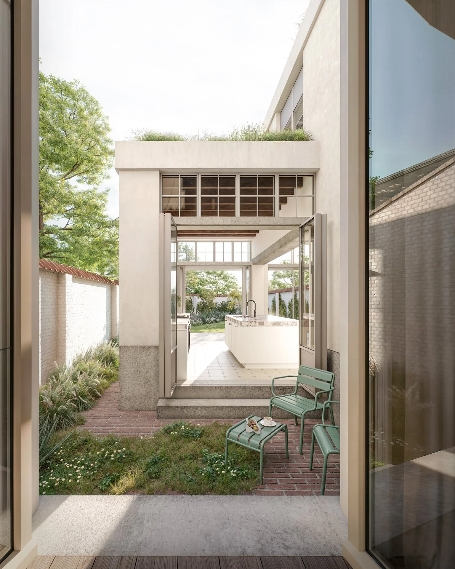 View from inside a modern home looking out through open glass doors to a backyard patio with two green chairs and a small table on grass and brick pavers. Beyond is a kitchen with white cabinets and an island, and a backyard with trees and a lawn.