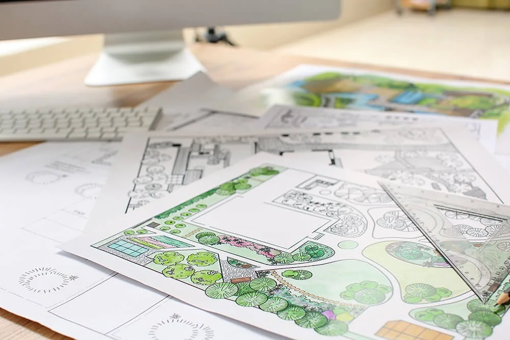 Garden design sketches spread on desk with computer in background