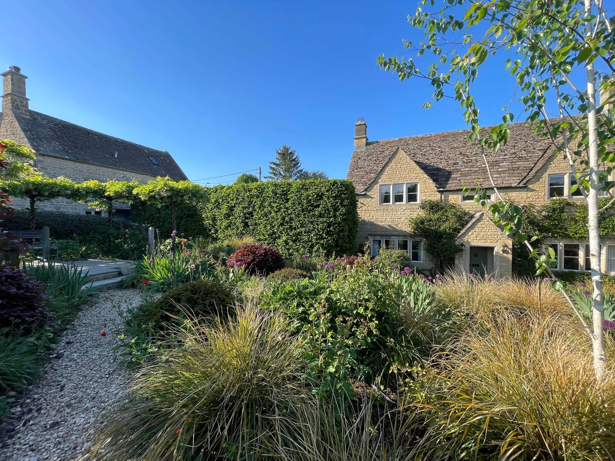 Large mature garden in Windrush with vibrant perennial borders, shade-tolerant planting, established shrubs and traditional Cotswold stone cottage