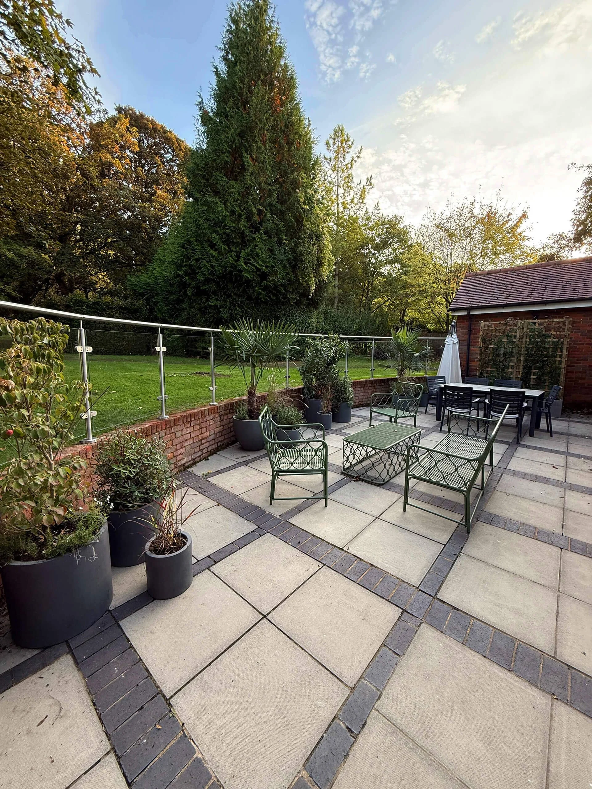 Paved patio with layered container planting and a glass balustrade in a suburban Hertfordshire garden designed and built by Vivid Gardens.