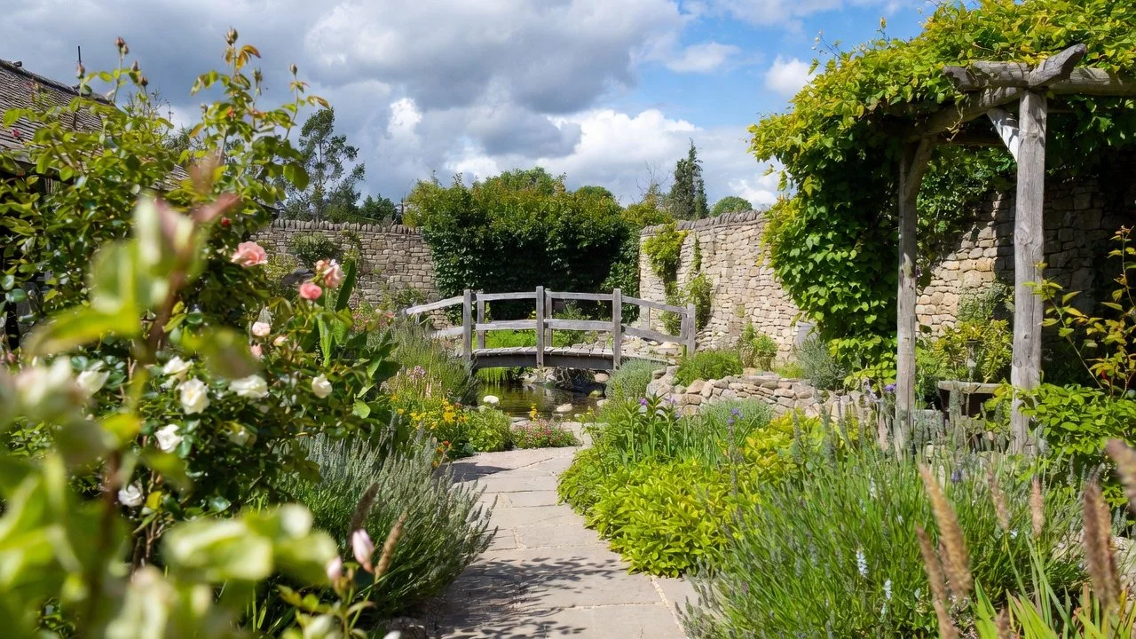 Oxfordshire garden with a stone path, planted borders and a timber bridge over water