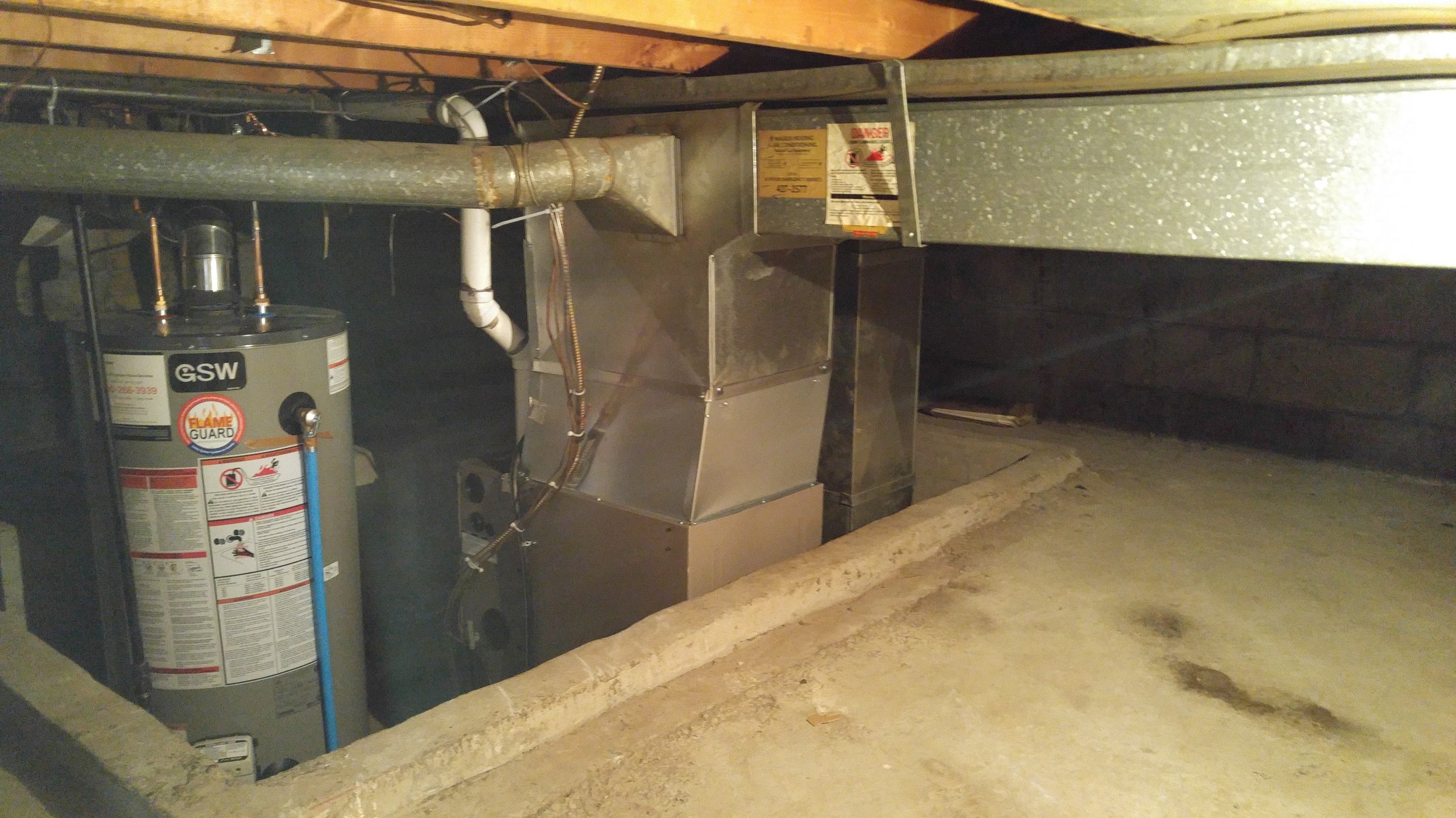 An underfloor view showing a water heater, HVAC ductwork, a metal air register, and a concrete floor in a crawl space.