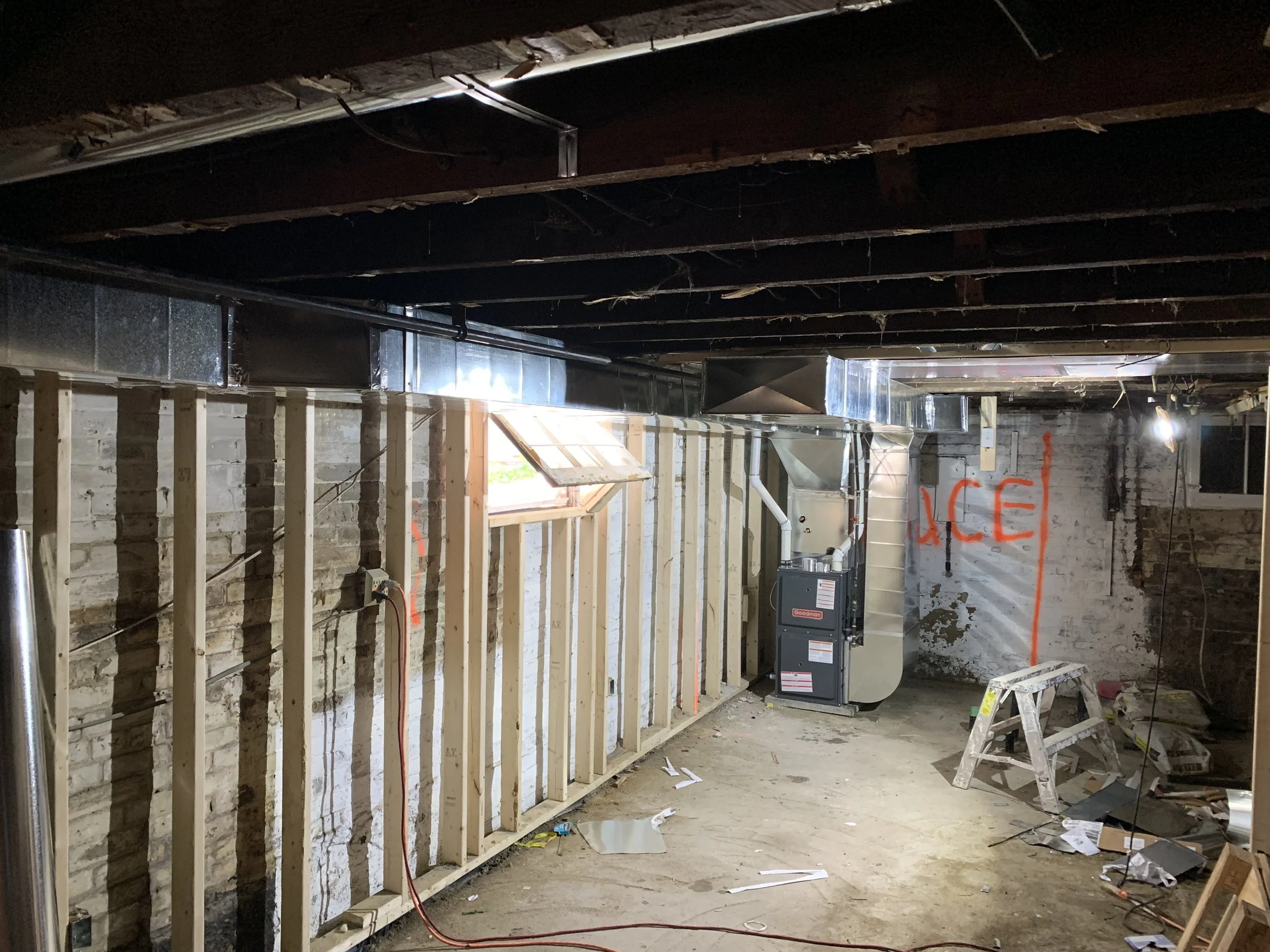  unfinished basement with exposed wall studs, insulation, HVAC system, and construction tools and materials scattered on the floor.