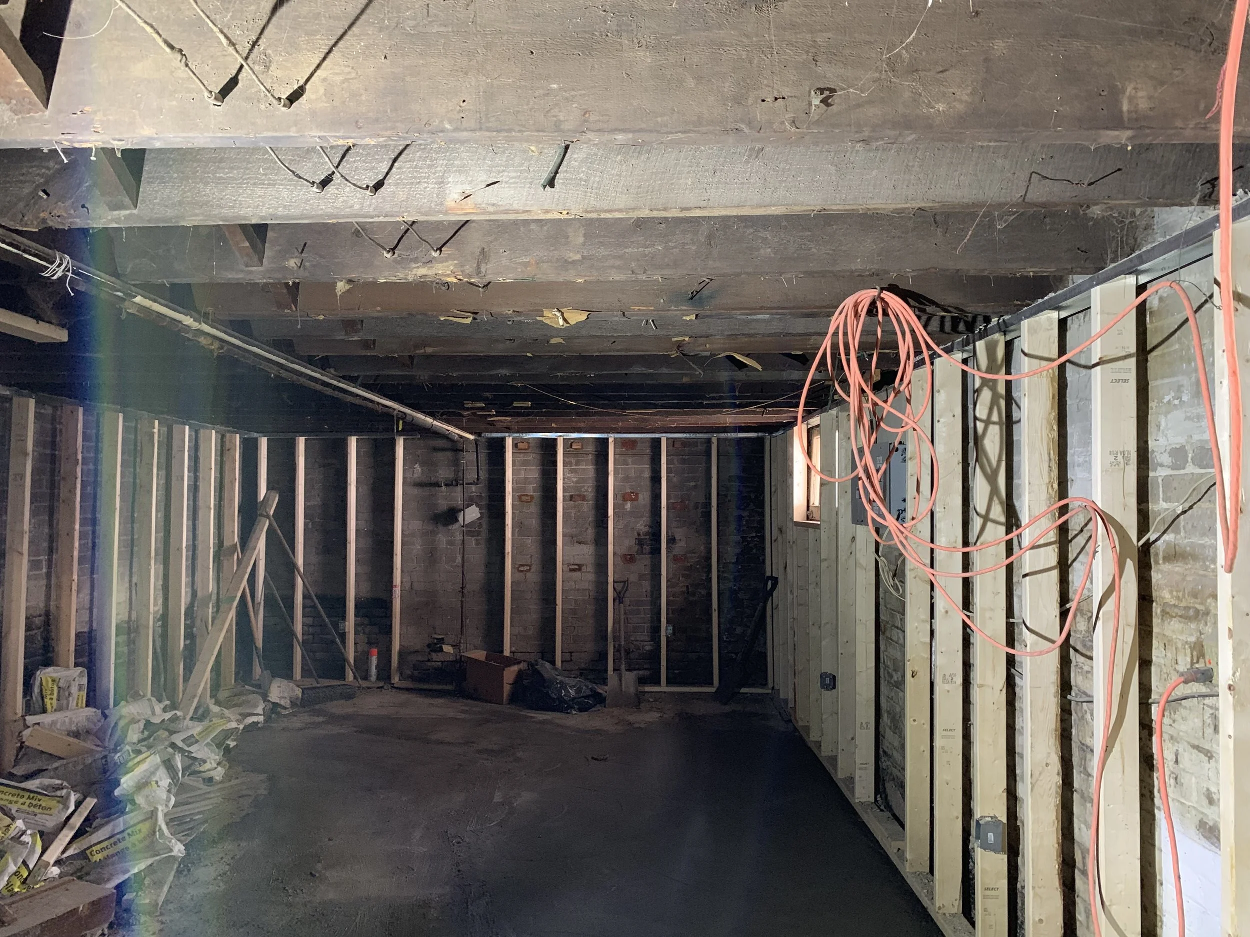 Interior of a room under construction with exposed wooden studs, electrical wiring, and construction materials on the floor.