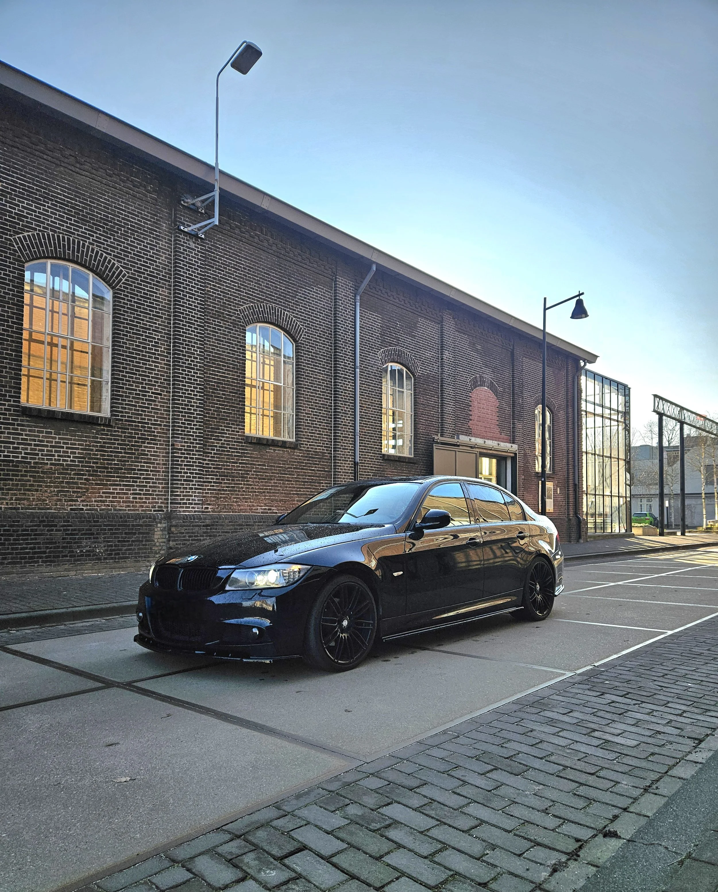 Een zwarte BMW-coupe geparkeerd op een parkeerplaats voor een bakstenen gebouw met grote ramen.