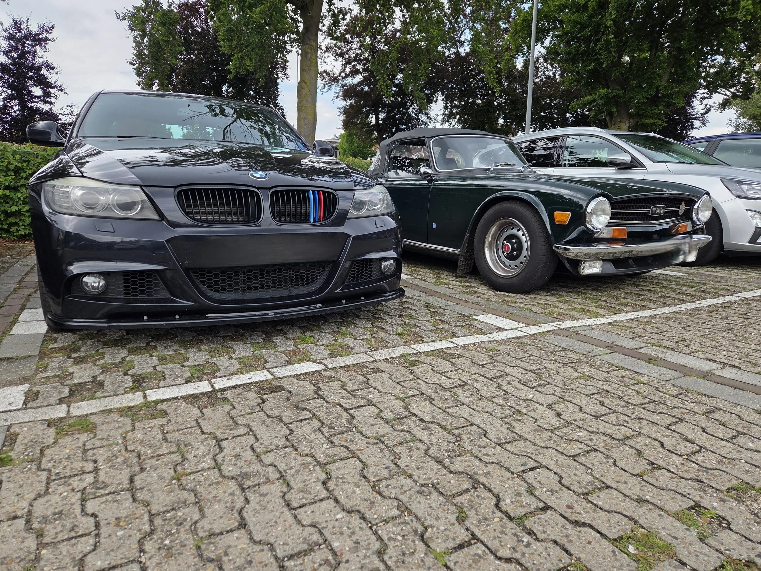 Twee auto's geparkeerd op een parkeerplaats, een moderne zwart BMW en een oude groene cabriolet