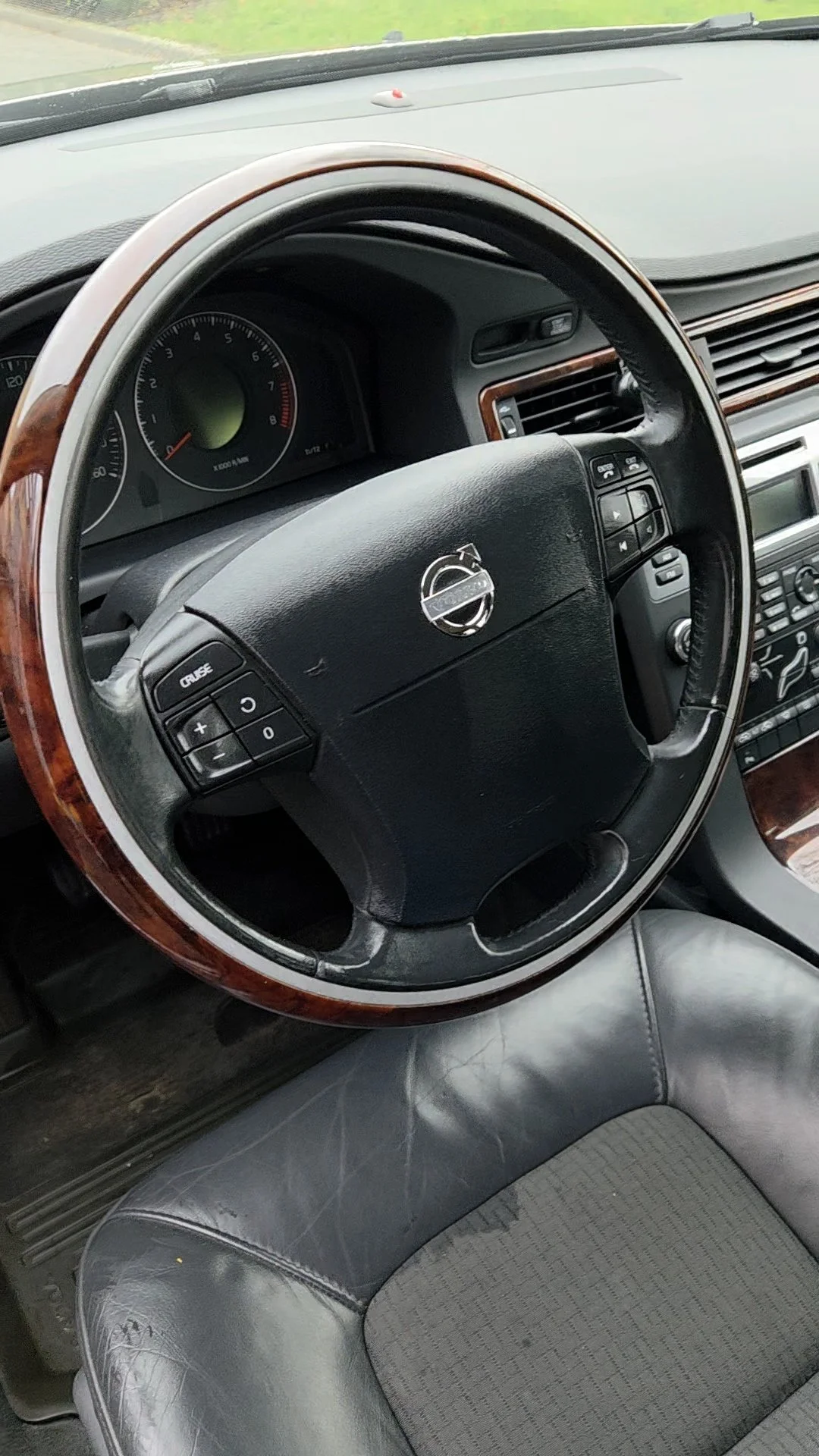 Interieur van een auto met een stuurwiel van Volvo met houten details, een snelheidsmeter en een dashboard.