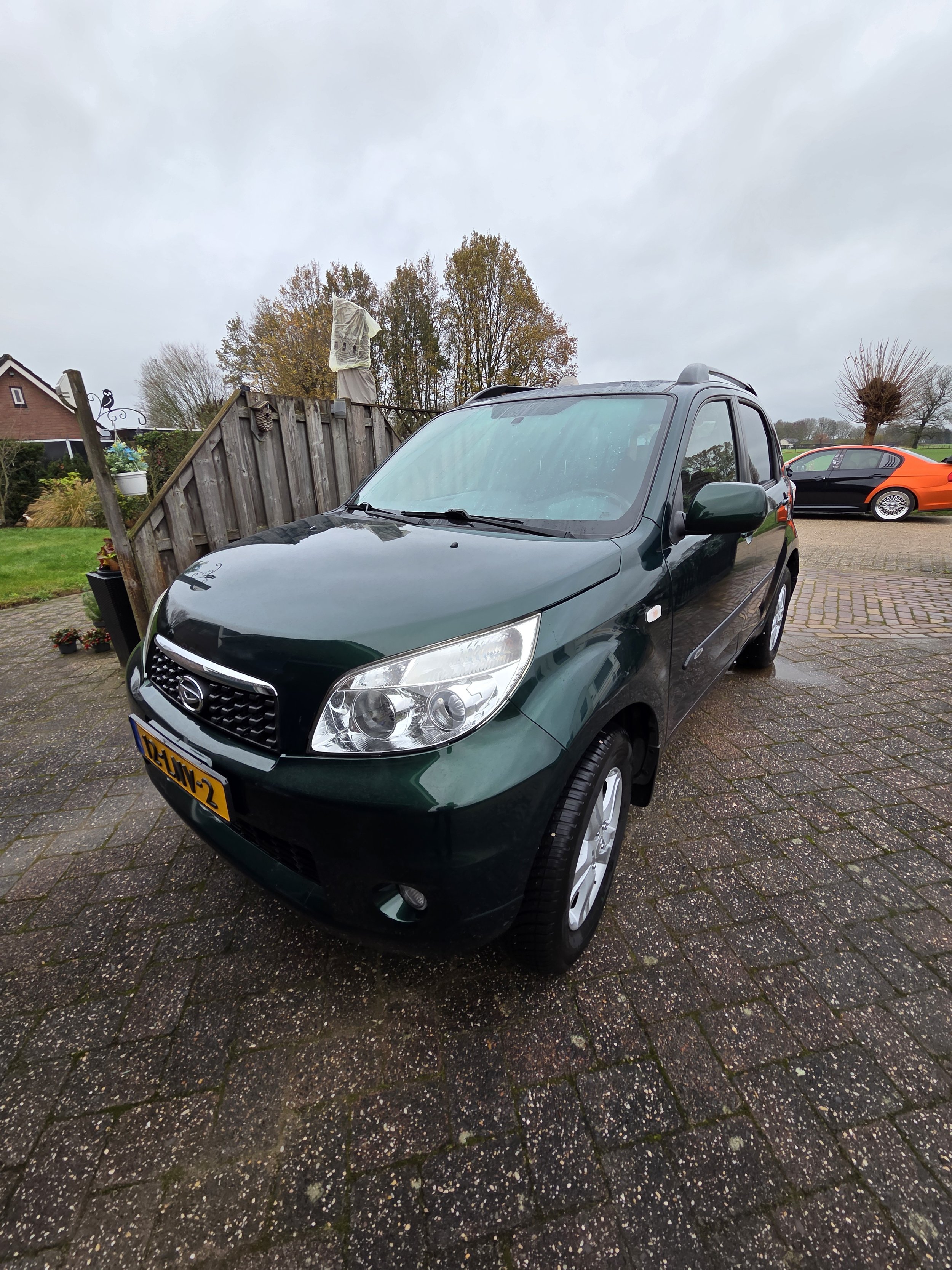 Groene Hyundai Getz auto geparkeerd op een oprit, met een houten schutting en andere auto's op de achtergrond.