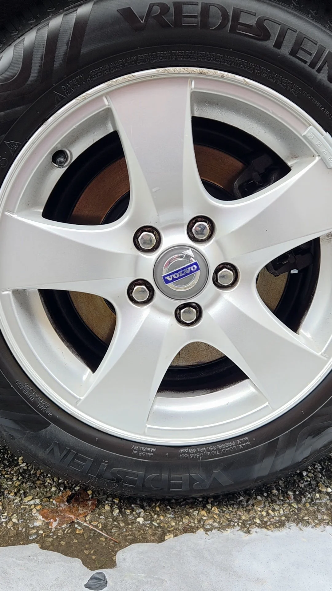 Een autoband en velg met het Volvo-logo in het midden, gelegen op een ondergrond met stenen en een paar bladeren.