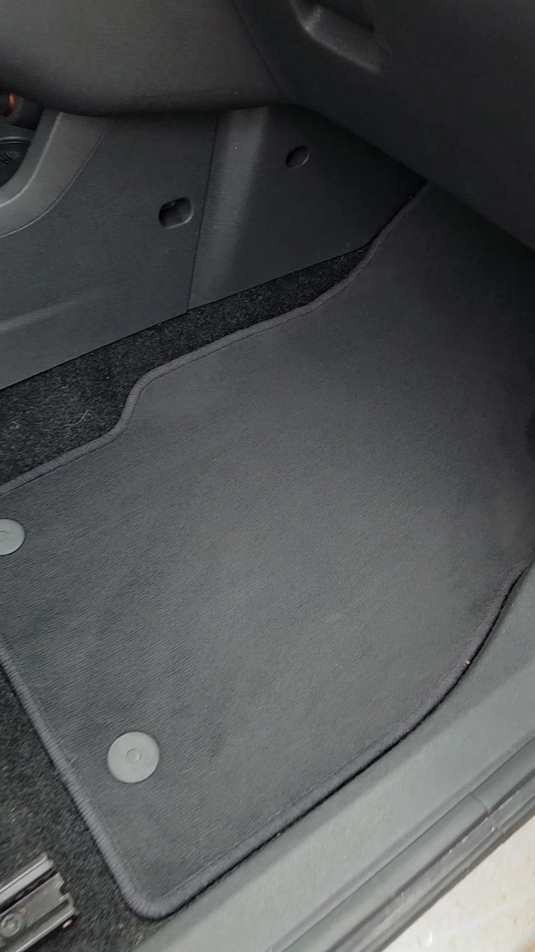 De afbeelding toont de vloer van een auto, inclusief een lichtgrijze mat en delen van de zitting en de binnenkant van de deur die in zwart en grijs zijn.