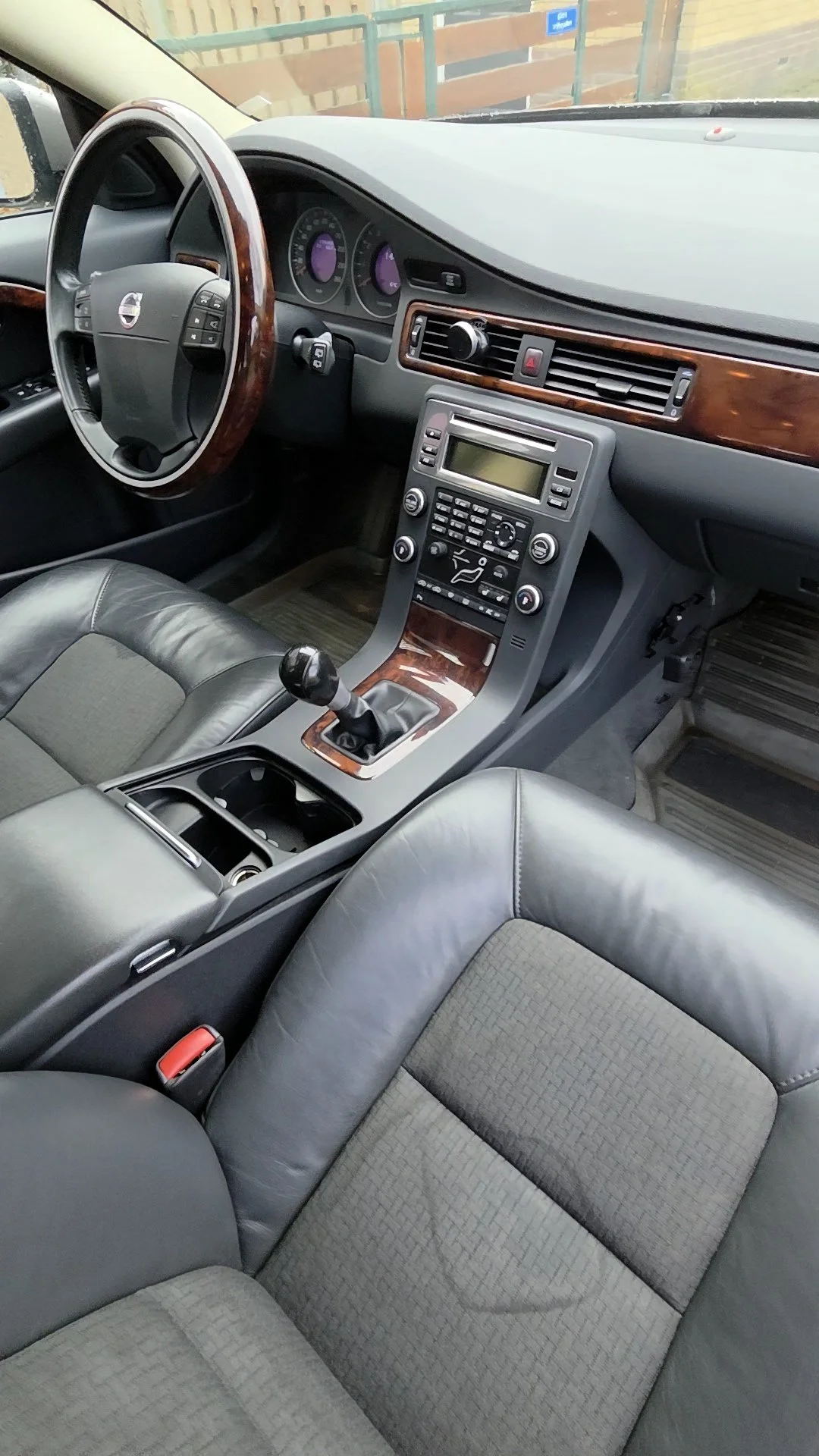 Interieur van een auto met leren stoelen, stuur met houtafwerking, dashboard, centrale console en handgeschakelde versnellingspook.