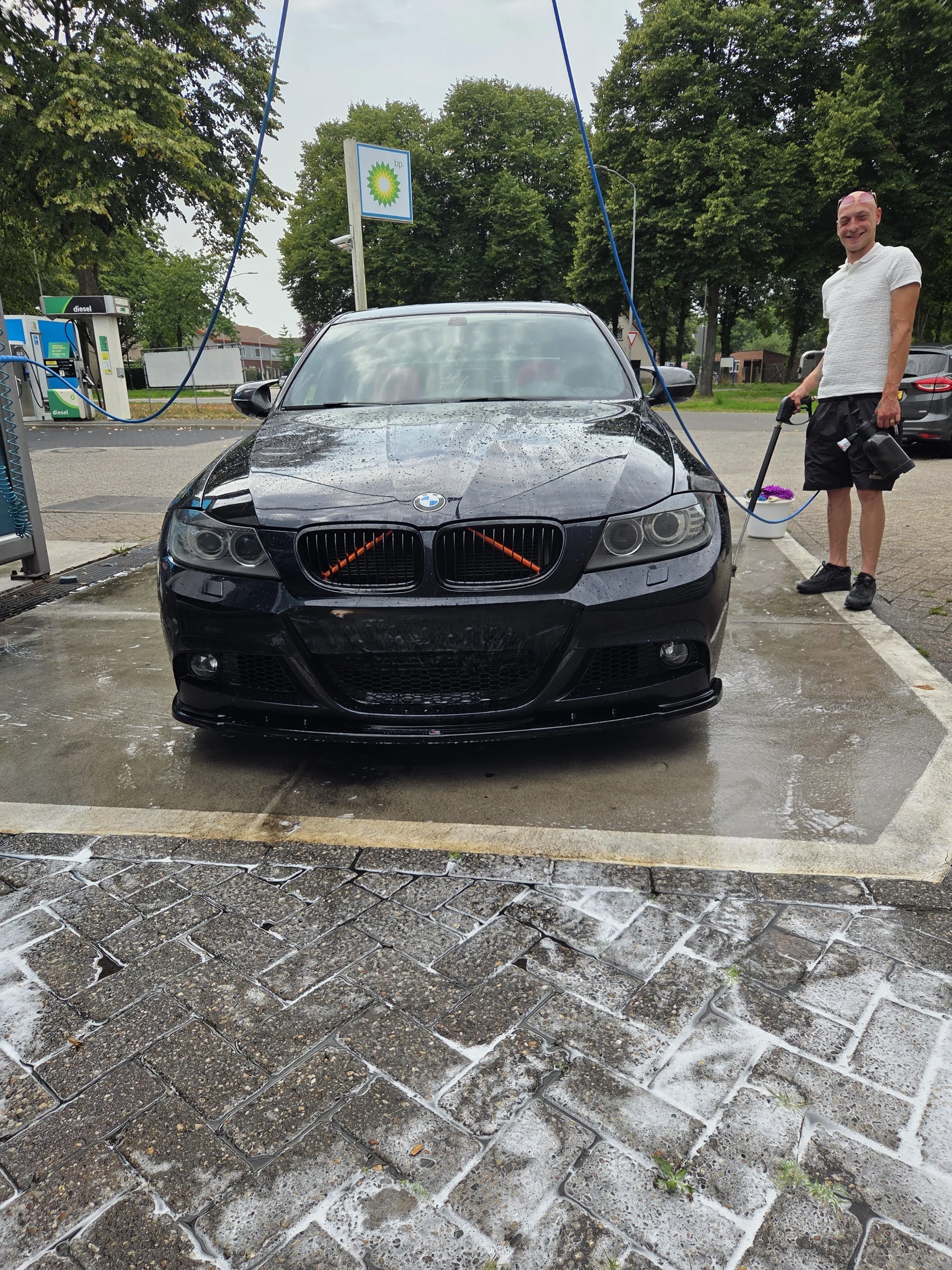 Man wast een zwarte BMW-auto bij een tankstation in de regen, terwijl hij zich voorbereidt op het wassen.