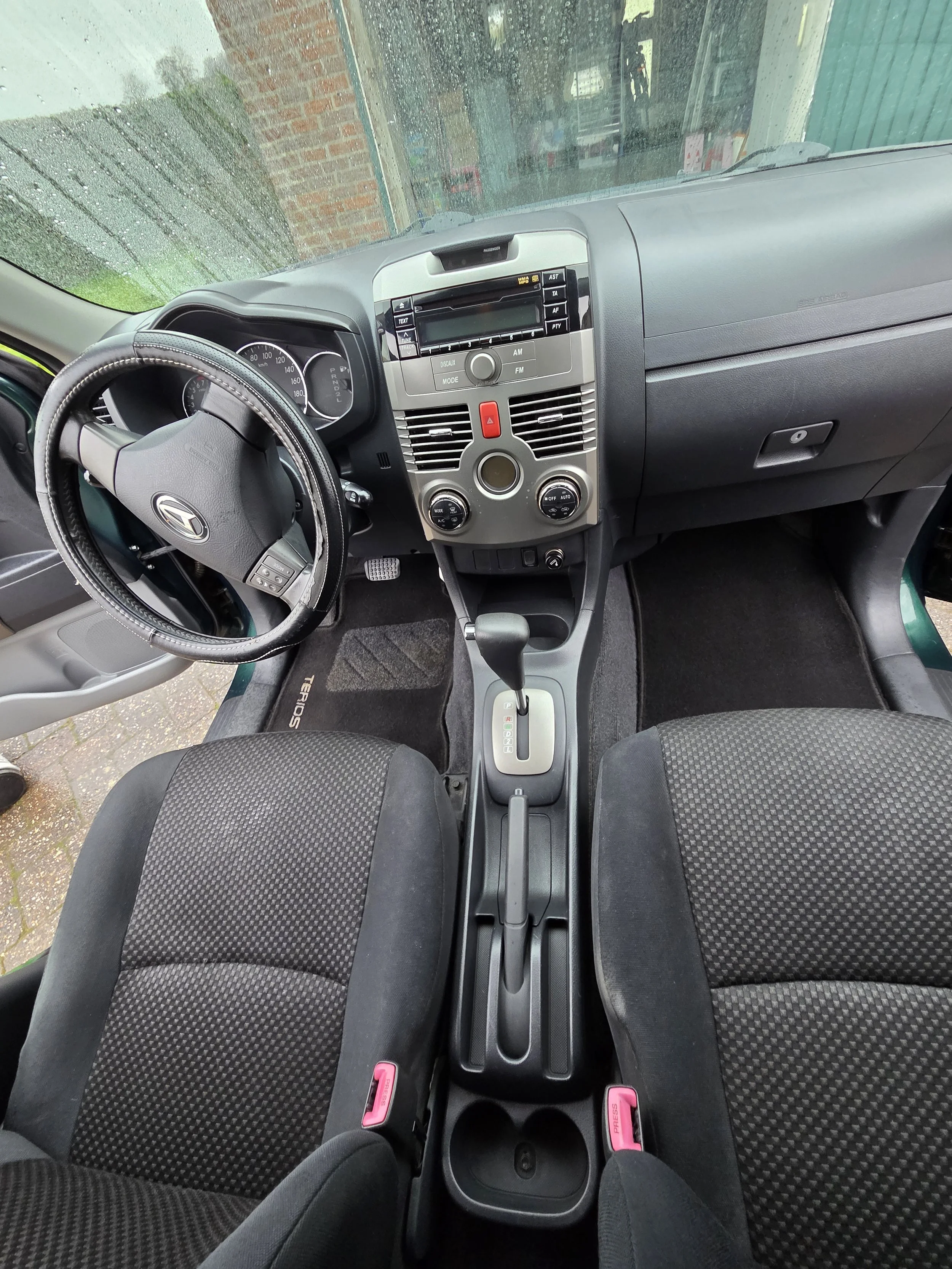 Interieur van een auto, inclusief stuurwiel, middenconsole met automatische versnellingsbak, twee voorstoelen en een dashboard.