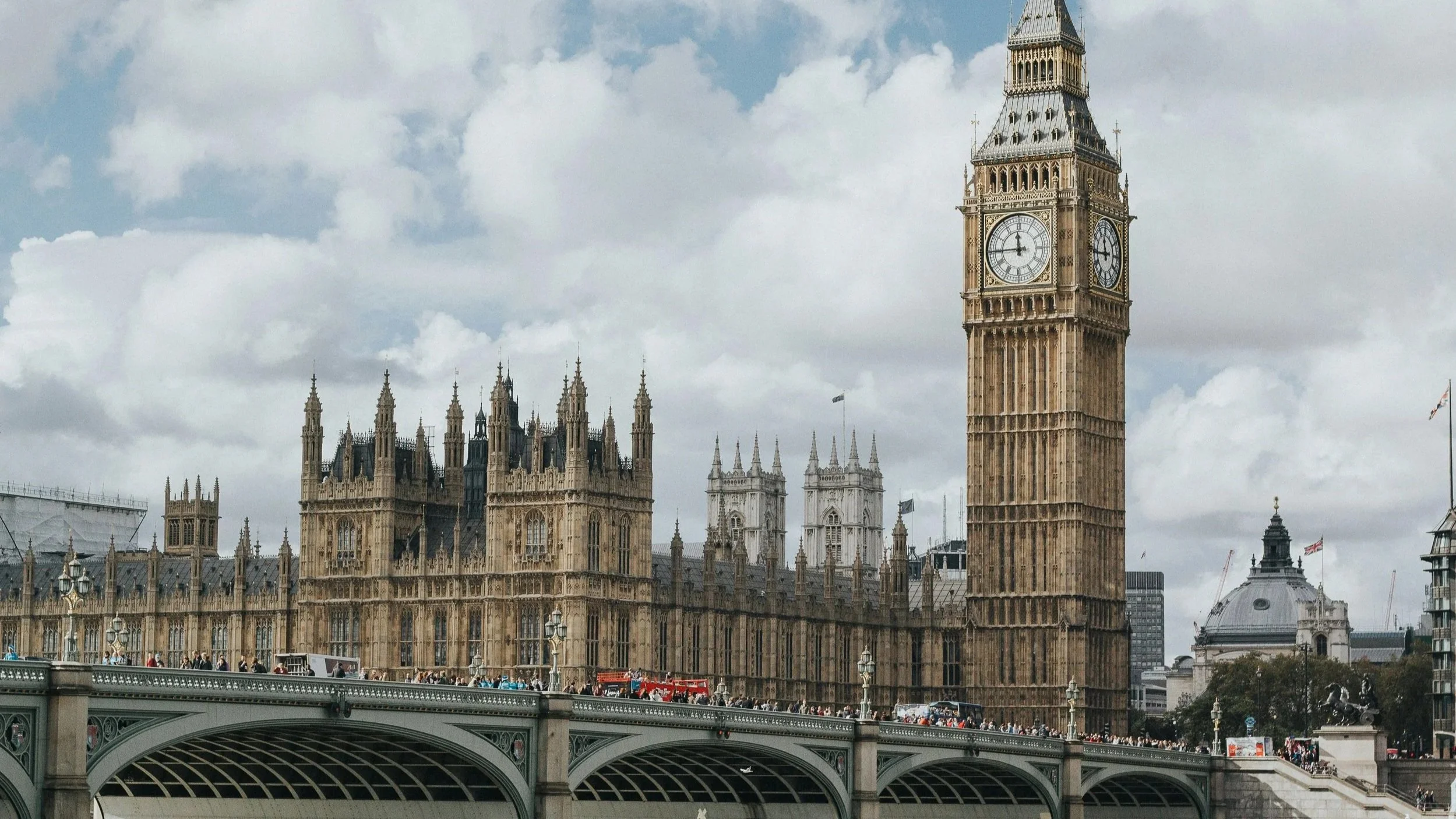 Big Ben clock tower and the Houses of Parliament in London seen from Westminster Bridge with cloudy sky above.