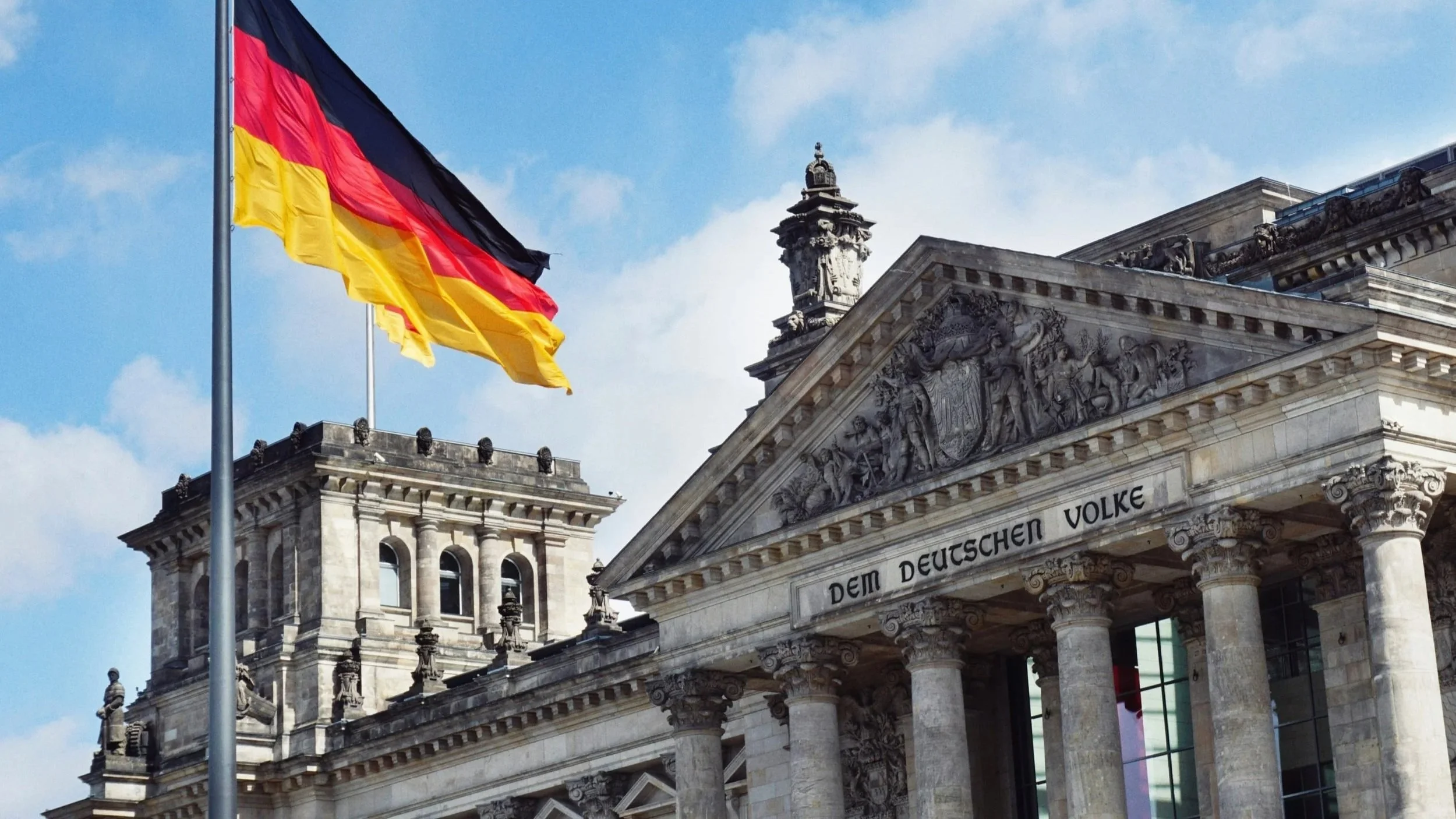 The Reichstag building in Berlin, Germany, with two German flags flying in the foreground.