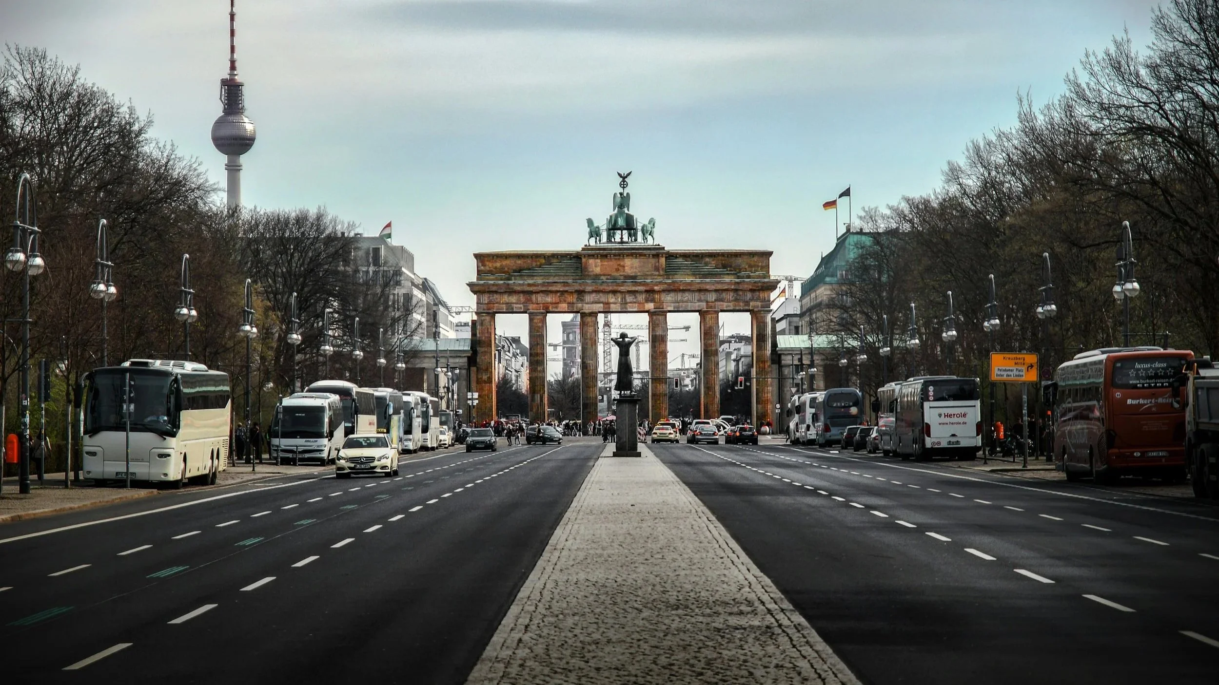 View of the Brandenburg Gate in Berlin, Germany, with traffic and buses on the street and trees on either side.
