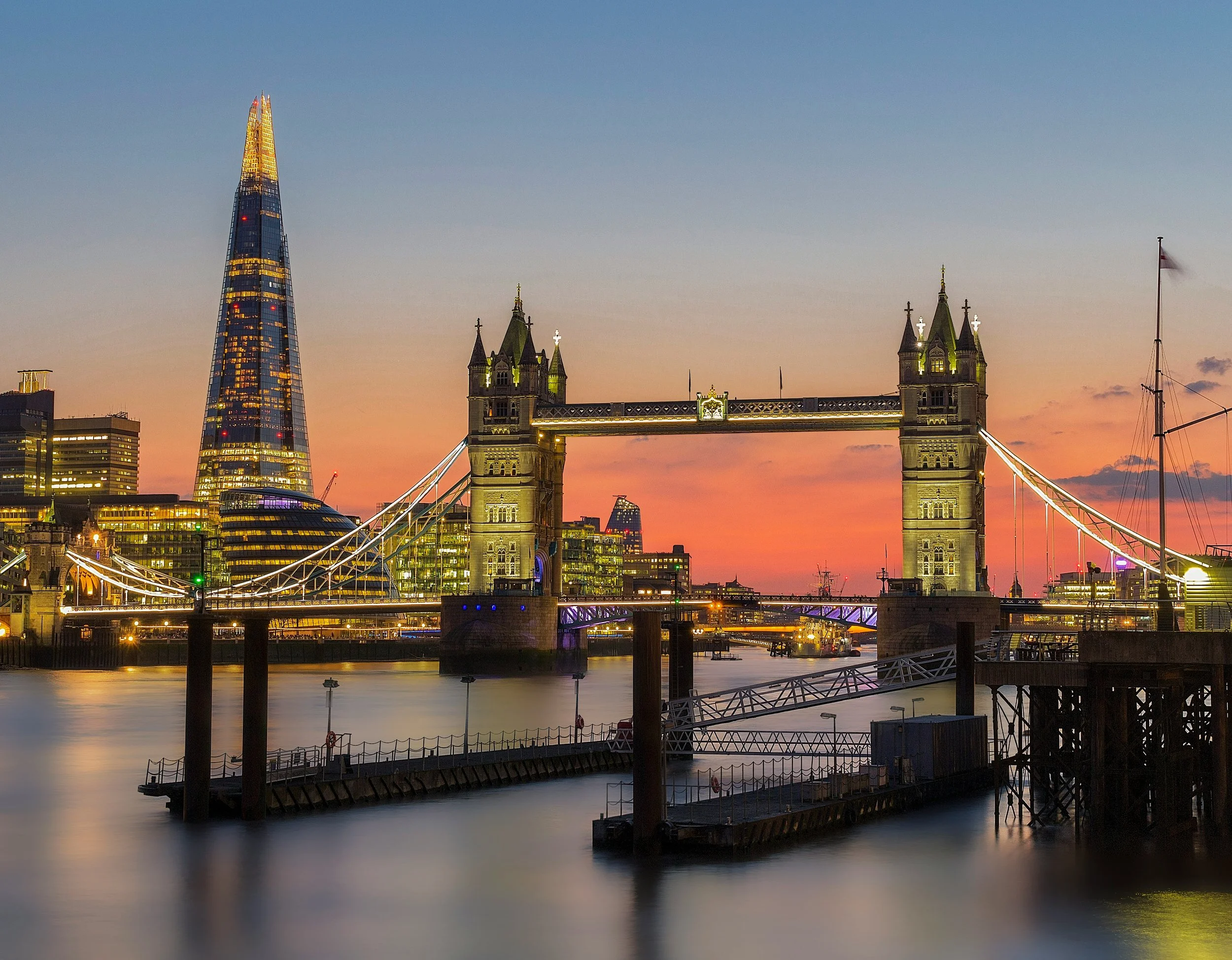 London skyline at sunset featuring the Tower Bridge and The Shard skyscraper.