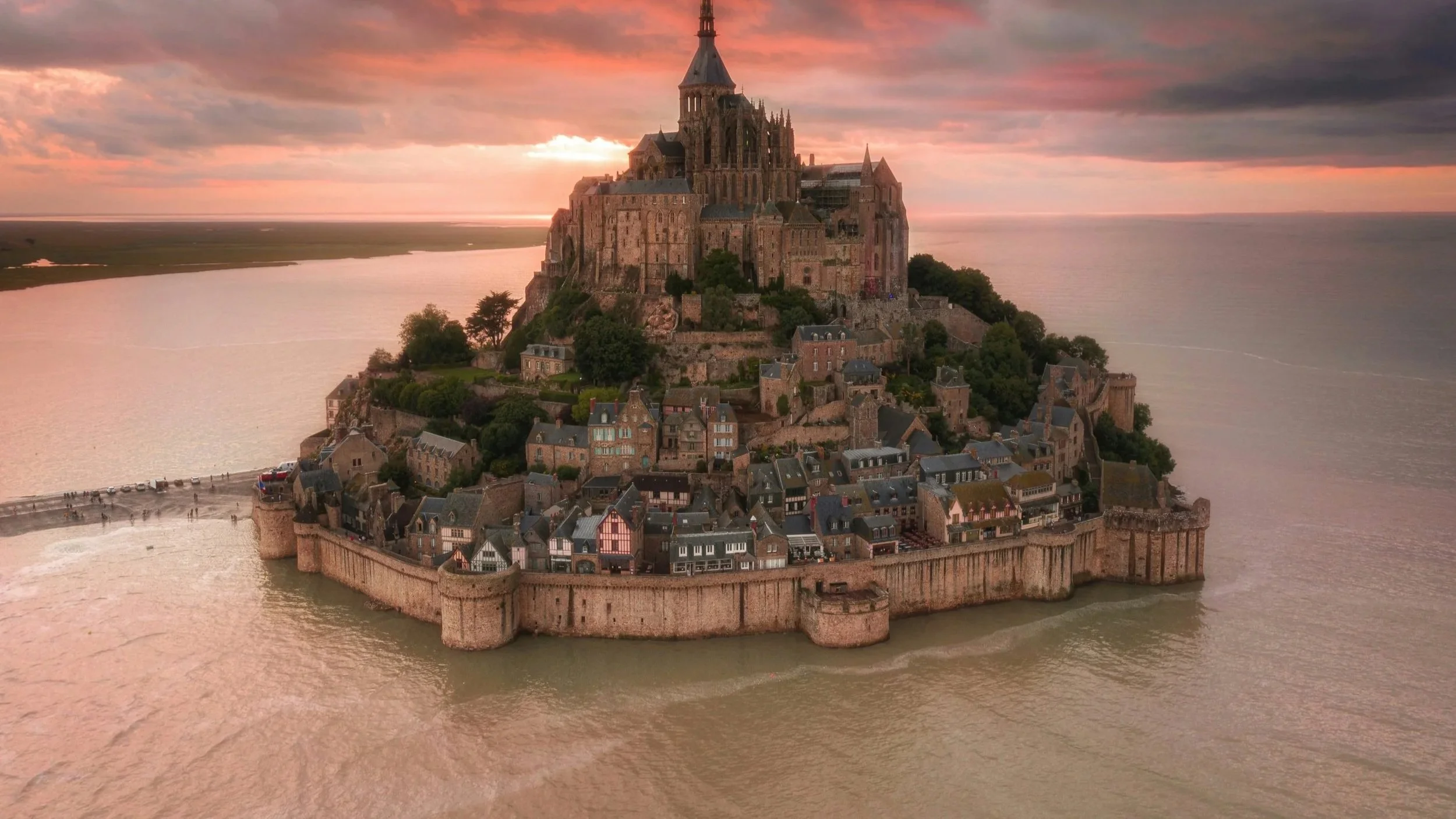 Aerial view of Mont Saint-Michel, a historic island commune in France, showing a medieval monastery and surrounding village during sunset.