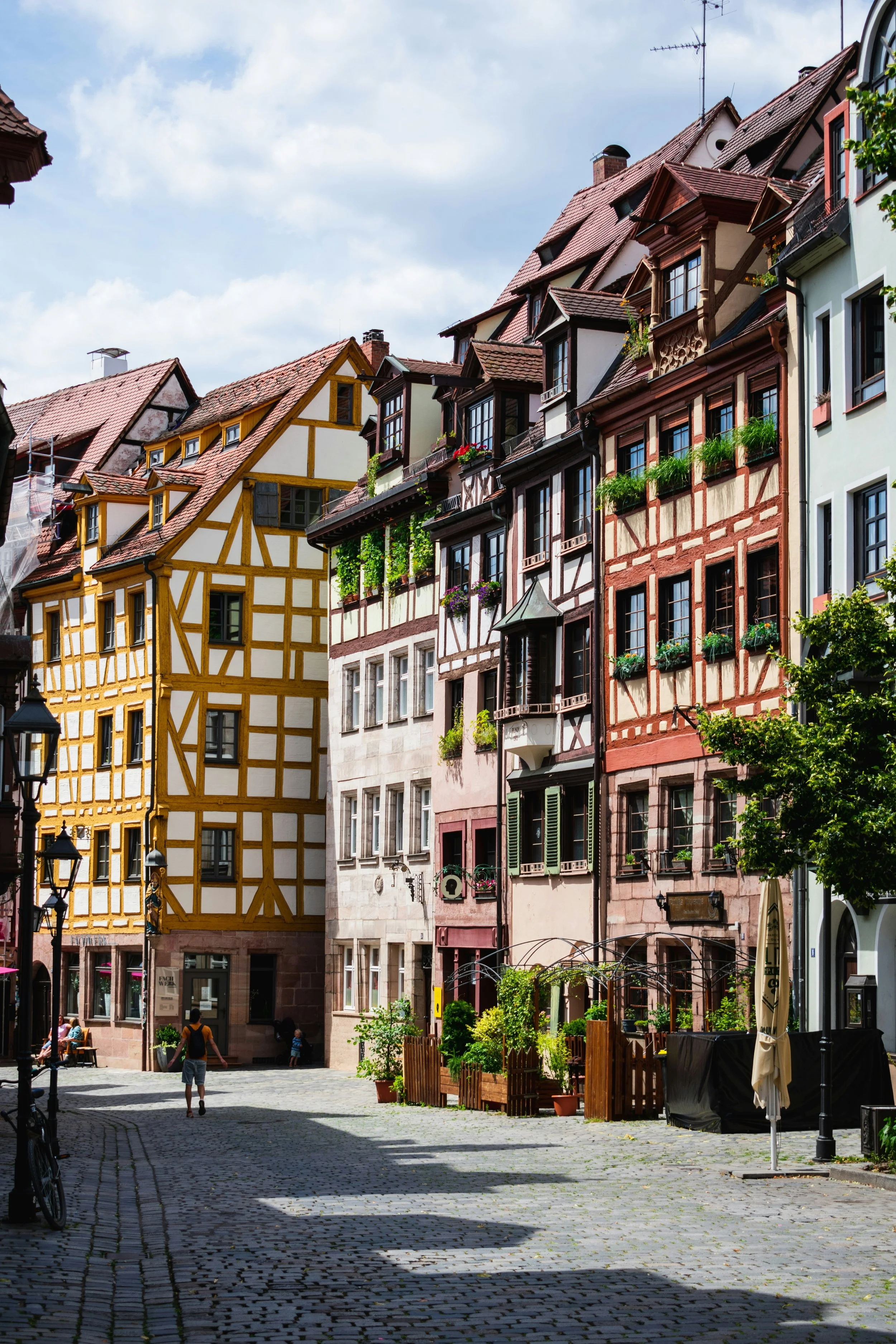 Colorful historic buildings with timber framing line a cobblestone street in a European city under a partly cloudy sky.