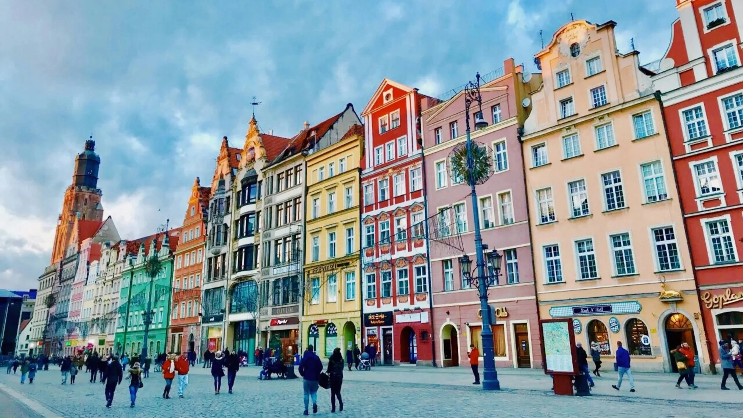 Colorful buildings with ornate architecture along a cobblestone street filled with pedestrians