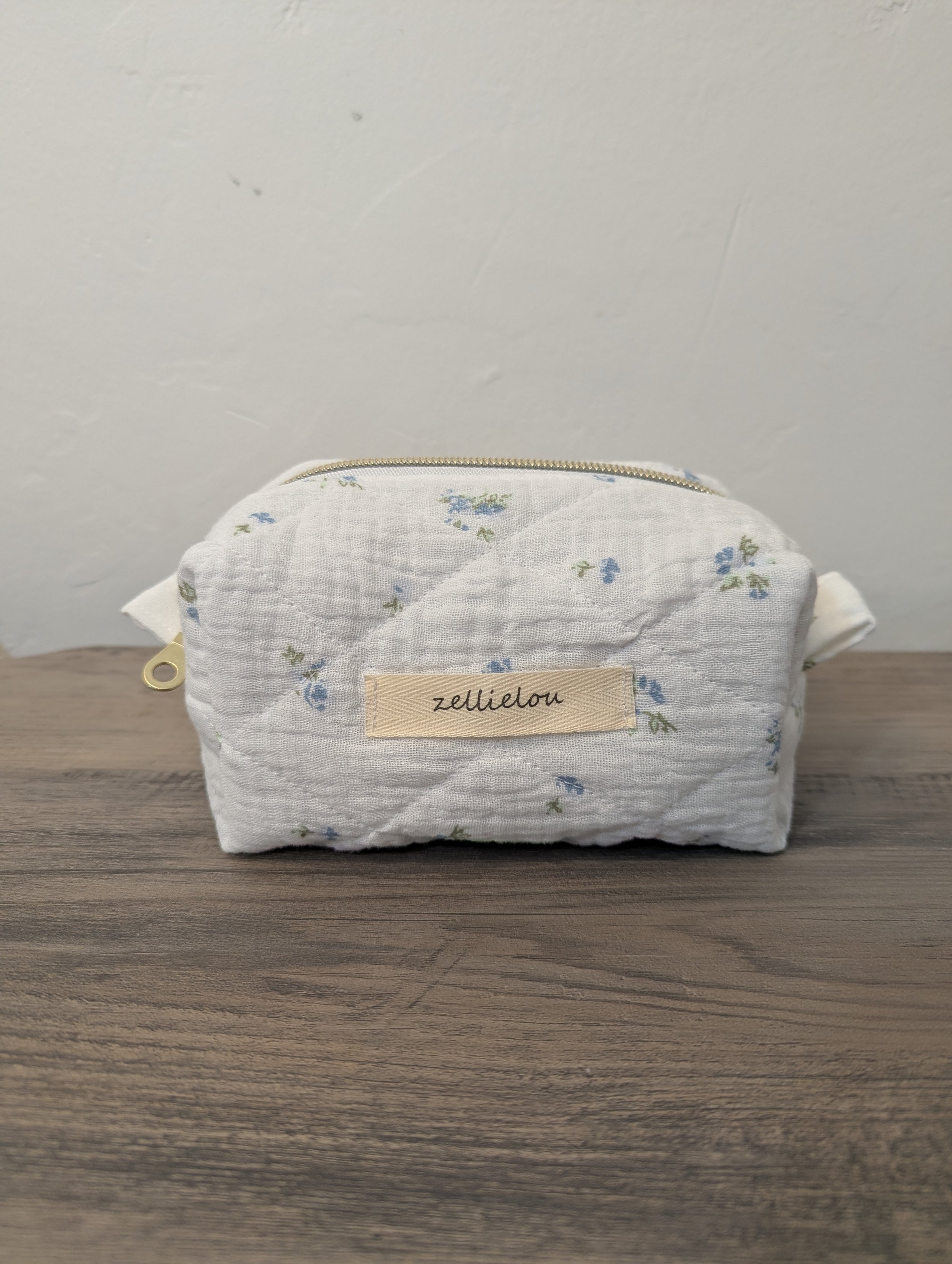 A small quilted fabric zippered pouch with a floral pattern.