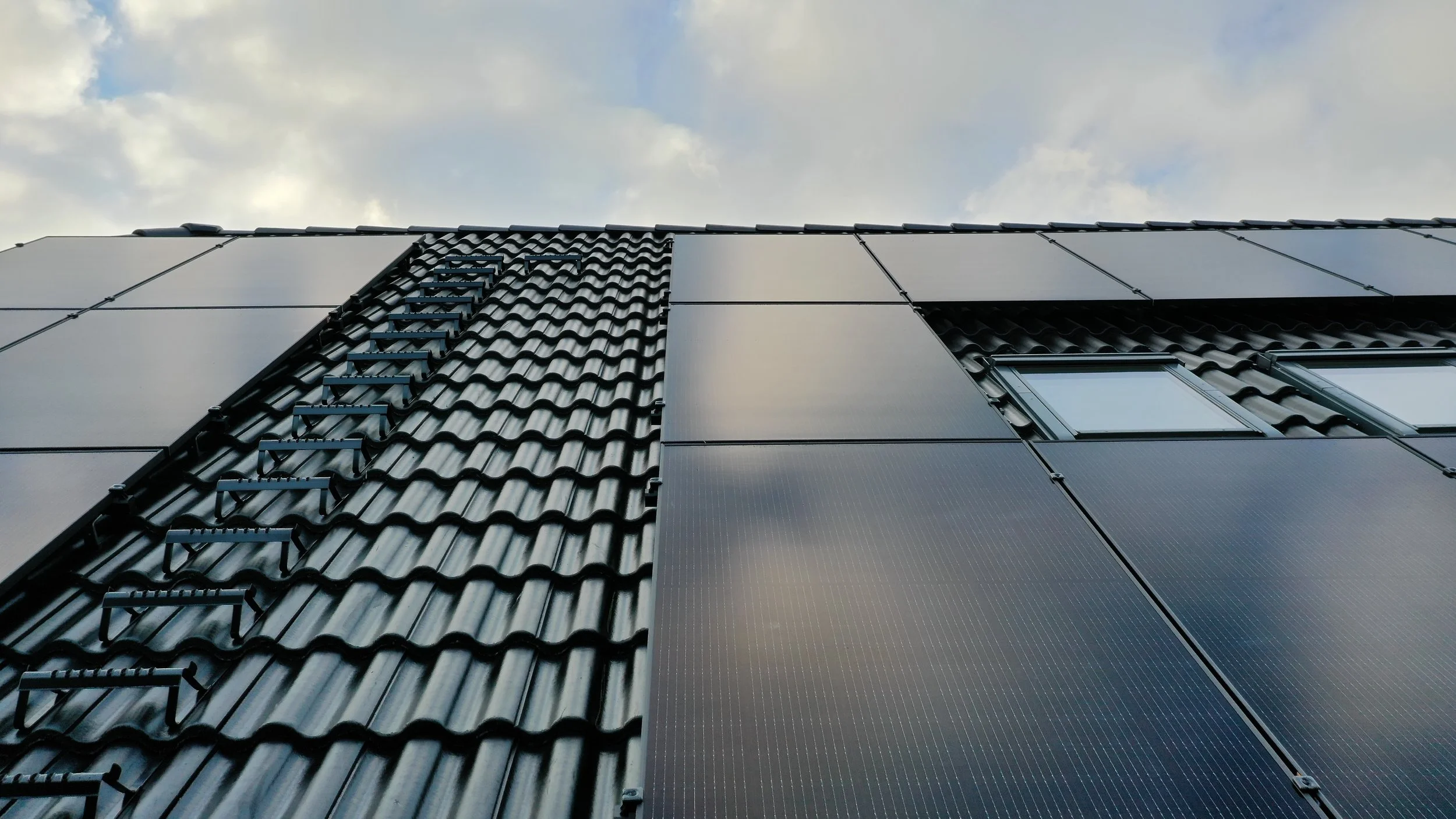 Bilder på ett tak med solpaneler på den högra sidan och traditionella takpannor på den vänstra sidan, med ett fönster mot högra sidan.