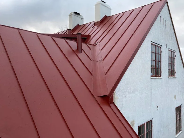 En vit villa med röd metalltak. Två skorstenar syns på taket och det finns tre fönster på gaveln.
