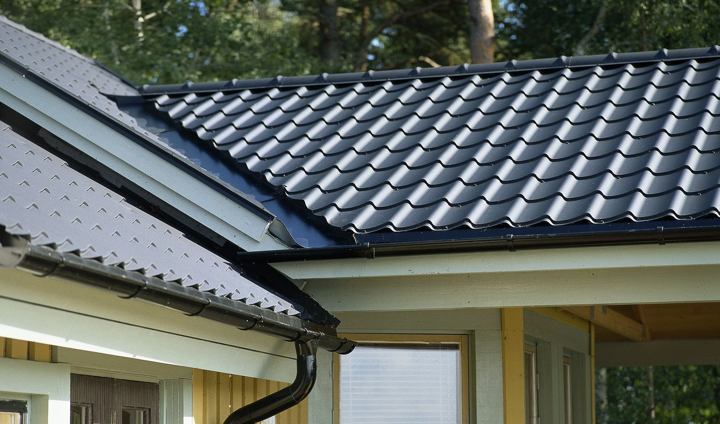 Bild av ett tak med olika typer av takpannor, inklusive betong och metall, på en liten byggnad, med träväggar och ett fönster.