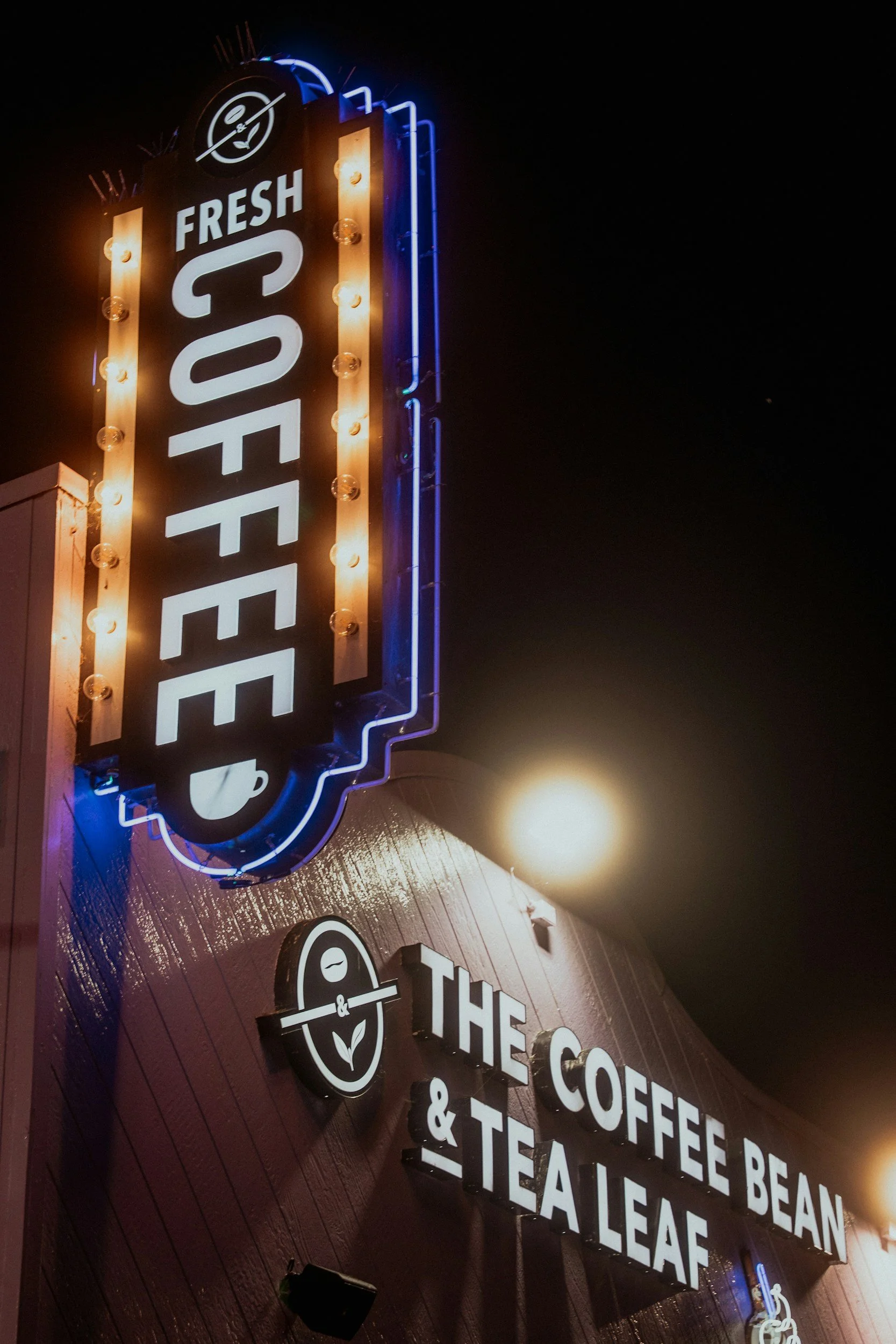 Neon sign advertising fresh coffee, tea, and leaf on a building at night.