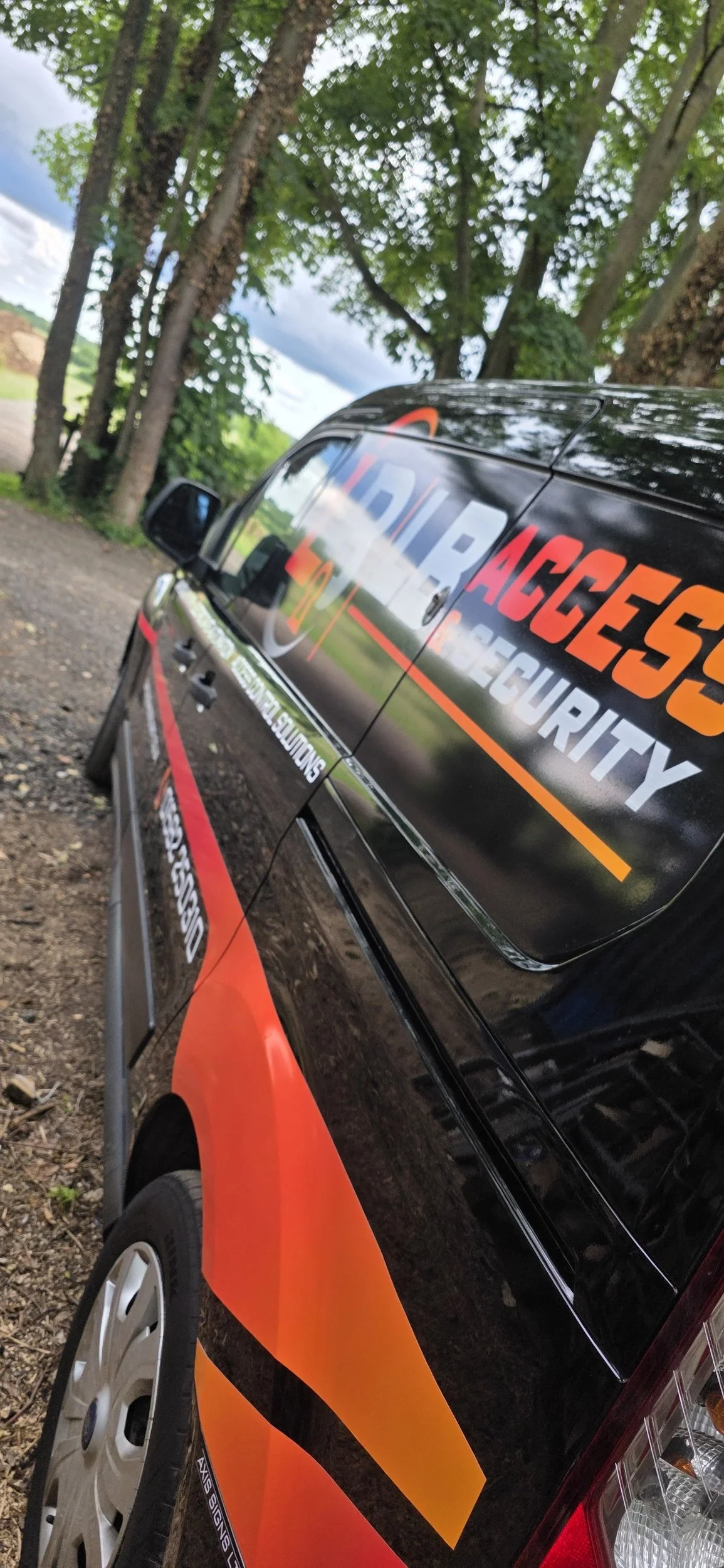 A black and orange emergency response vehicle with the words "LIBRAGES SECURITY" printed on the side, parked outdoors near trees and dirt ground.