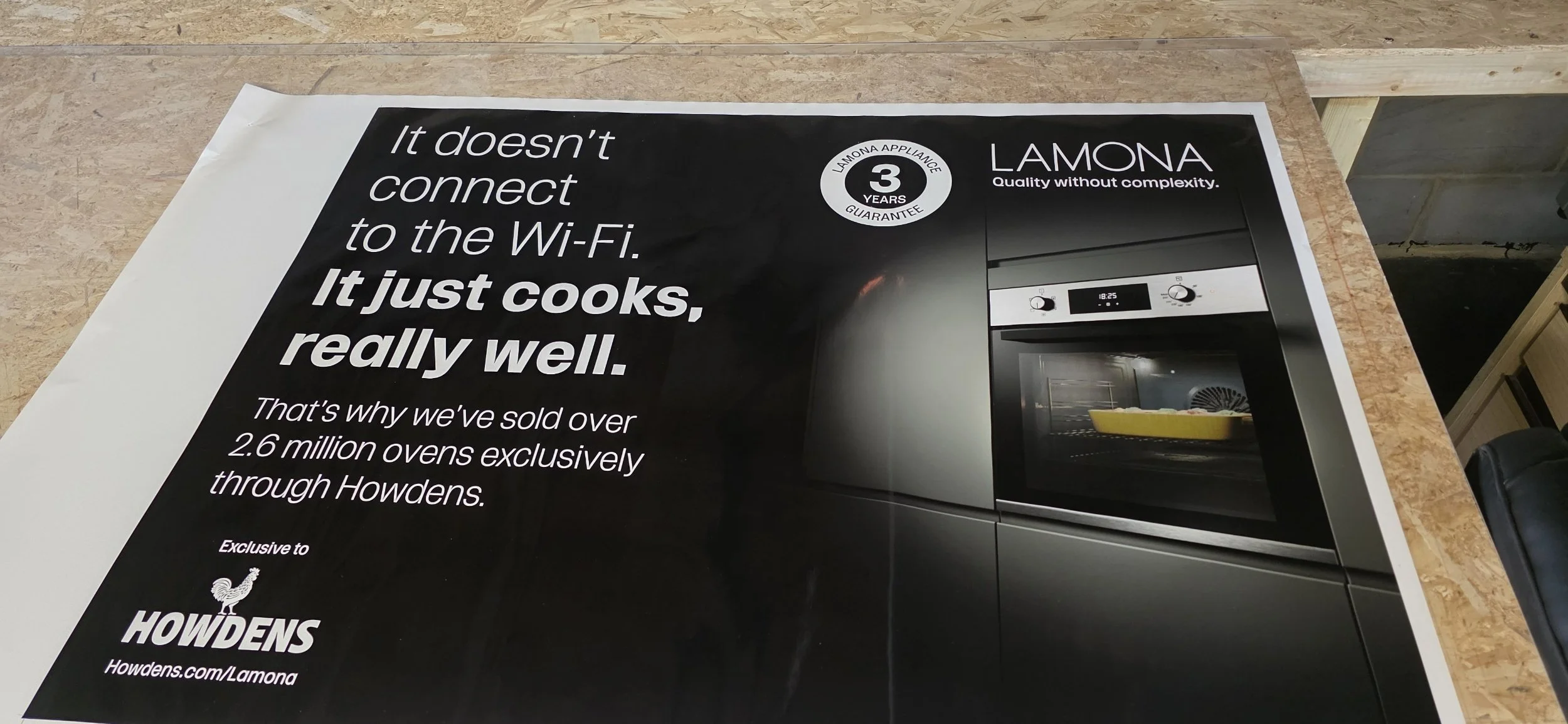 A promotional poster for Lamona appliances featuring a modern oven, with text emphasizing quality and a three-year guarantee, sold exclusively through Howdens.