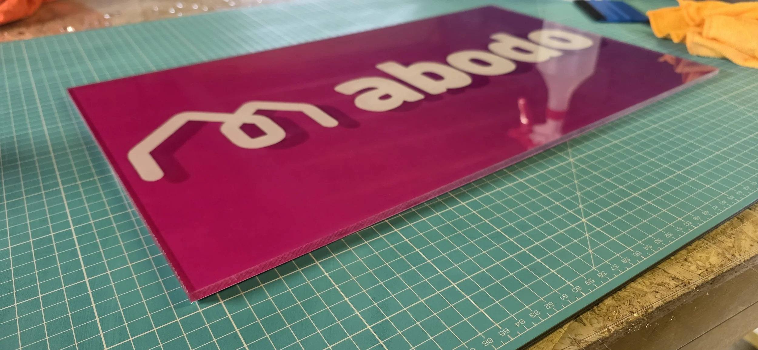 A pink acrylic sheet with white cutout text and a small house icon, placed on a green cutting mat.