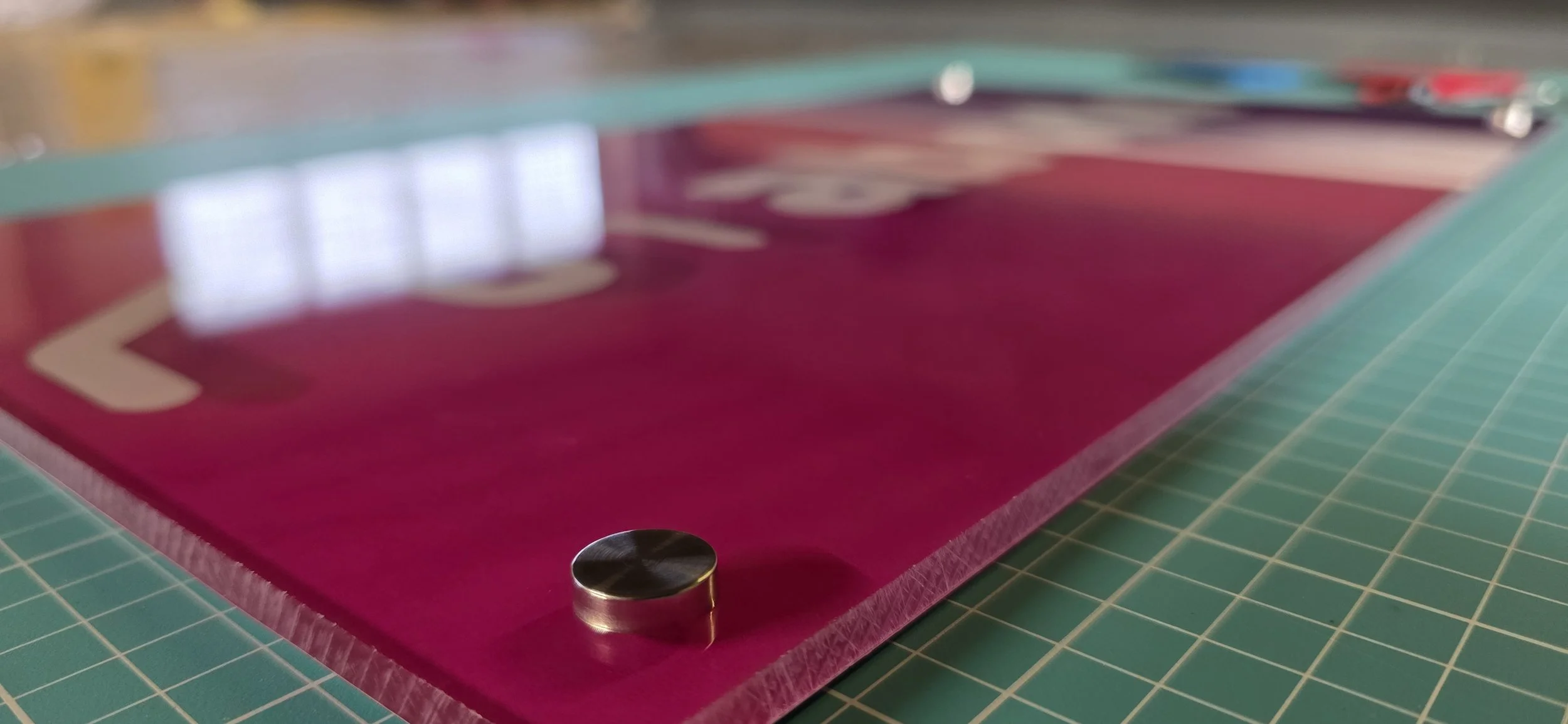 Close-up of a pink air hockey table with a single metal puck near the edge, on a green cutting mat.