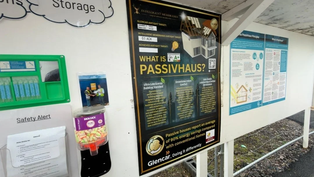 Poster explaining Passivhaus benefits, energy efficiency, and construction principles; safety alert document; container with multicolored candies; informational posters on building techniques.