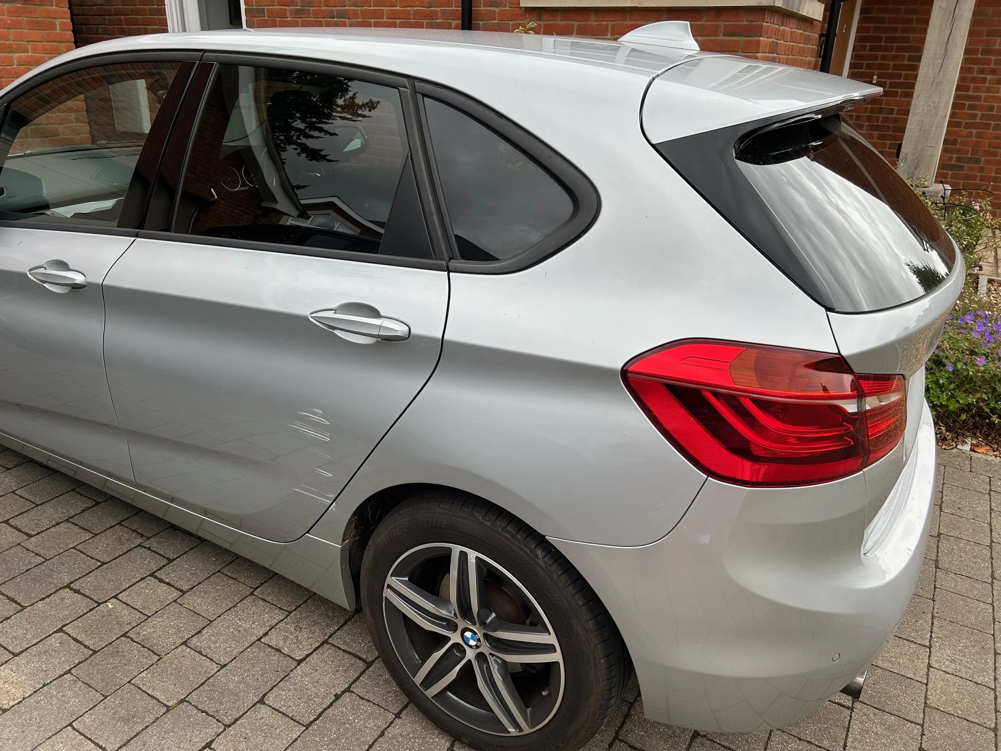 Silver BMW hatchback car parked on a brick driveway with some damage on the driver side door.
