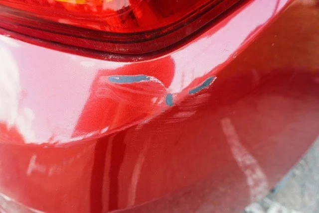 Close-up of a red car with a scratch and paint chip near the tail light.