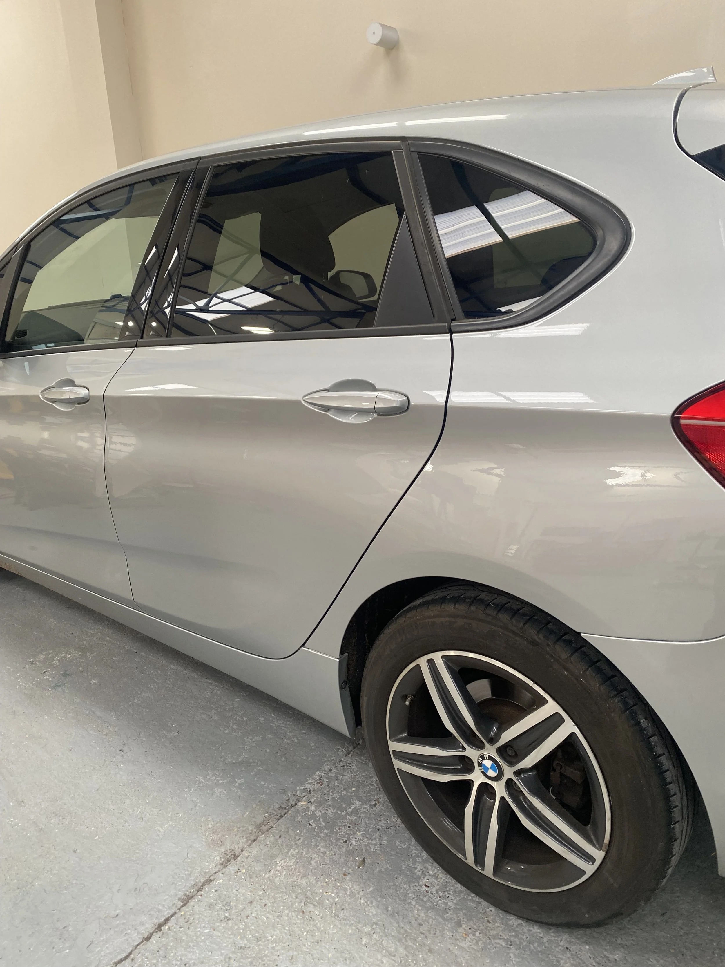 Silver BMW sedan parked in an indoor garage, showing the side view with tinted windows and alloy wheels.