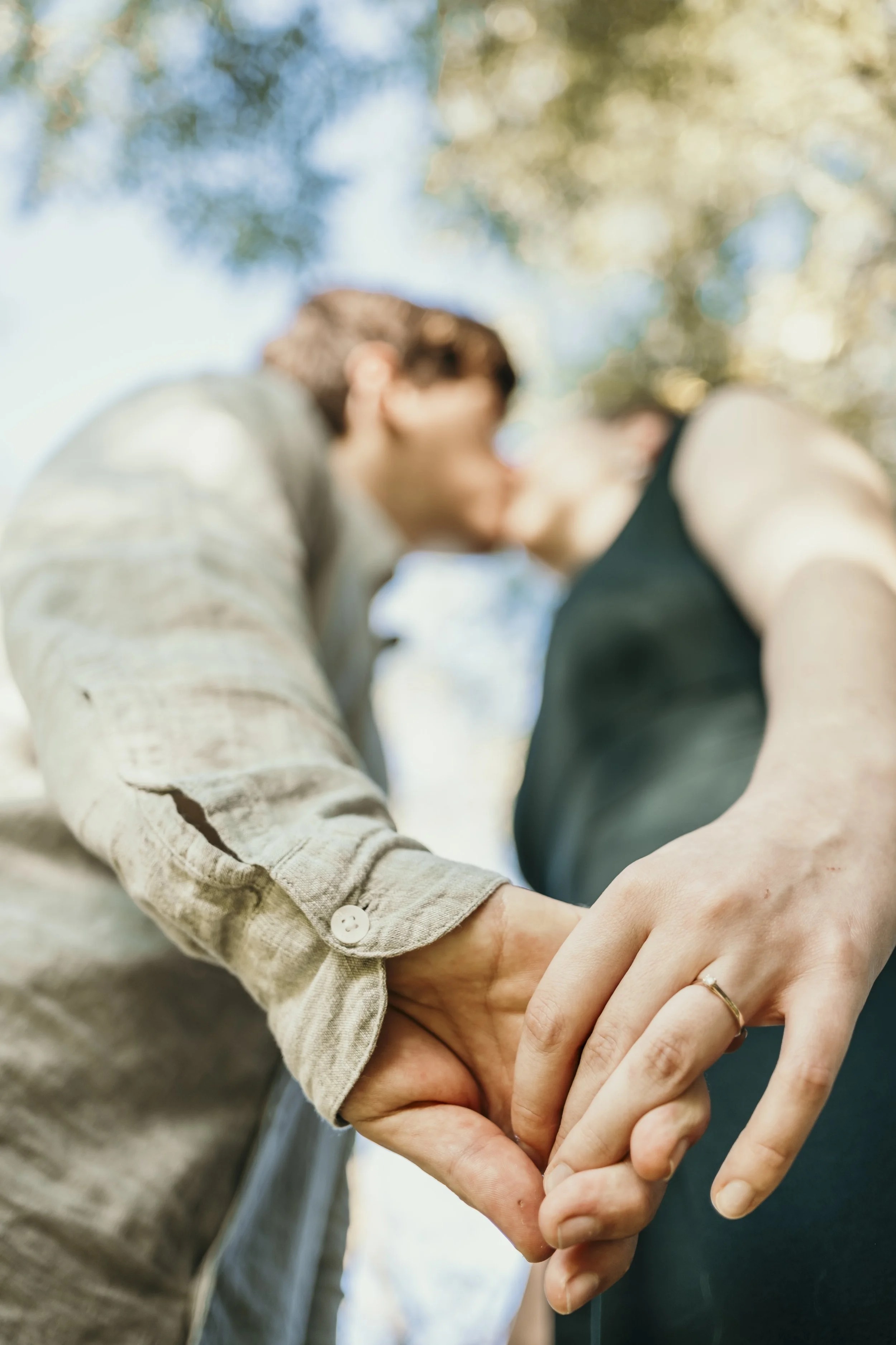 Un couple s'embrasse, se tenait la main, en plein air avec un ciel clair et arbres en arrière-plan.