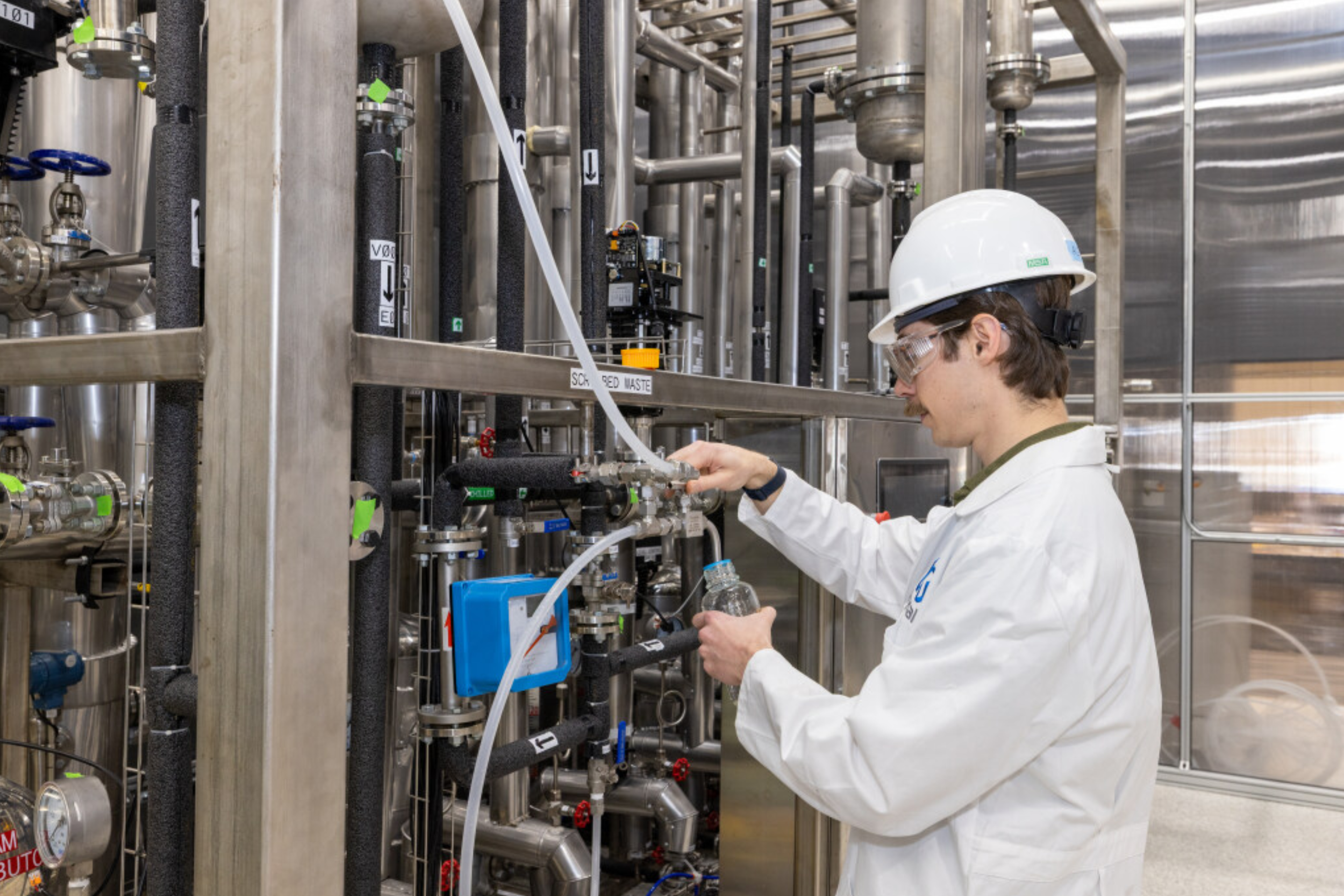 A scientist in safety gear working with industrial equipment in a laboratory or manufacturing setting.