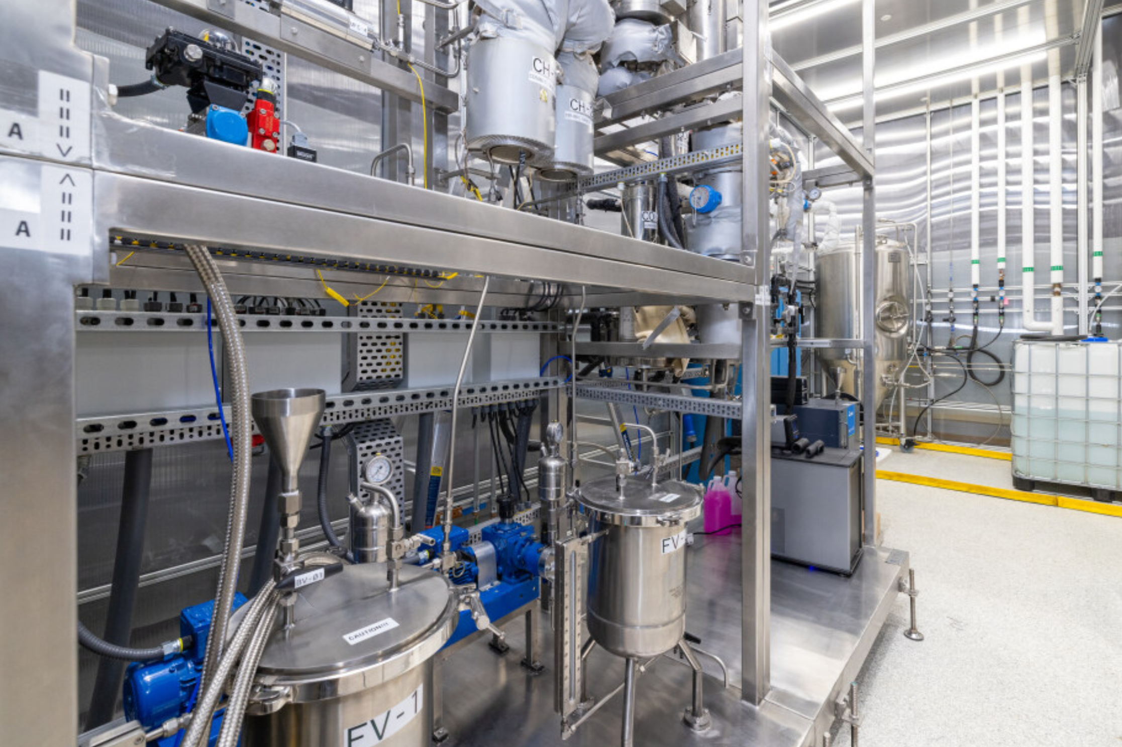 Industrial laboratory equipment with stainless steel tanks, pipes, and controls on a clean, bright floor.
