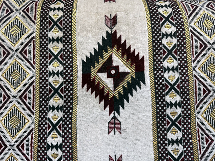 Close-up of a patterned textile fabric with geometric designs in black, white, yellow, and maroon, featuring a central diamond motif with arrows.