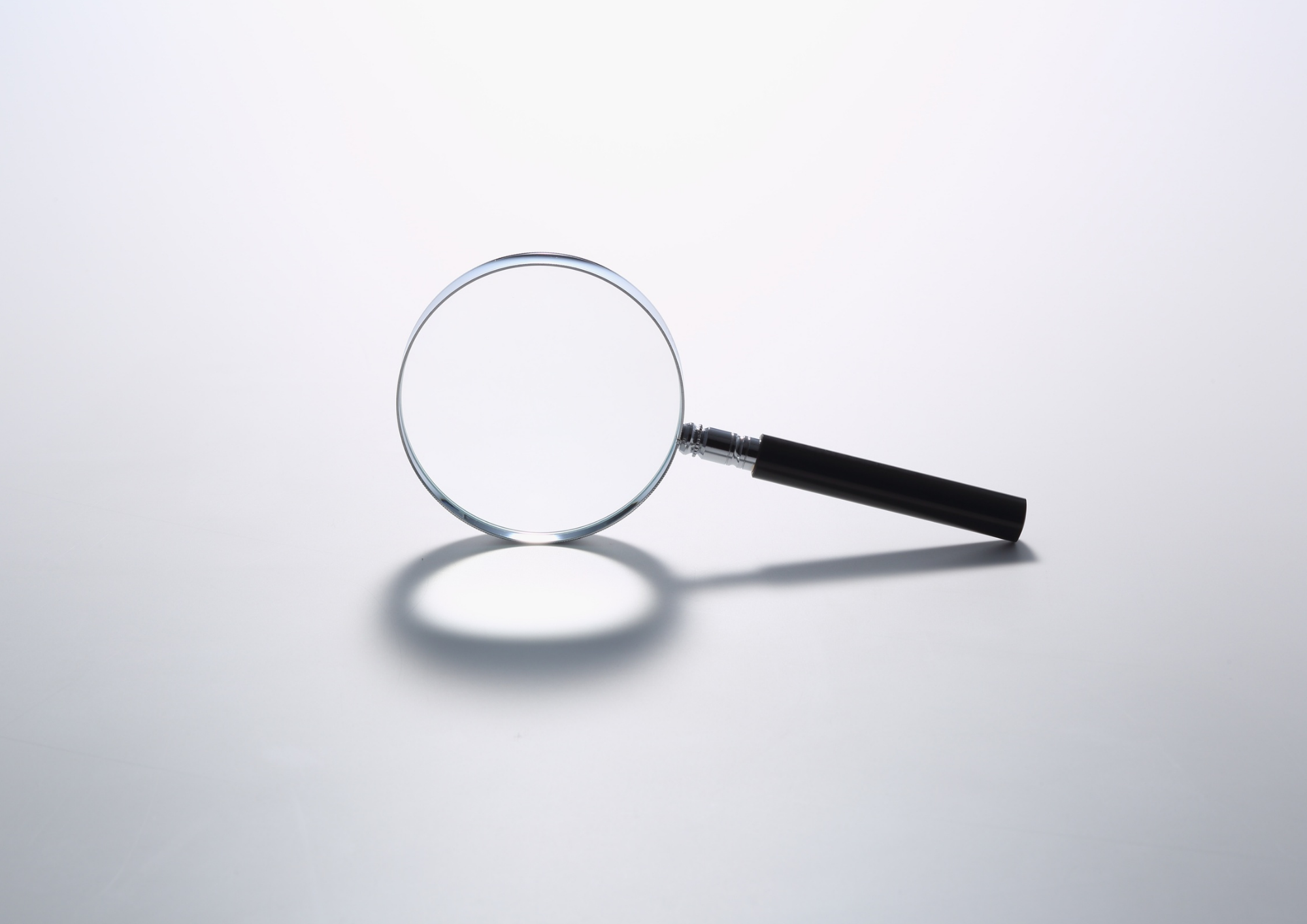Magnifying glass resting on a white surface, casting a shadow.