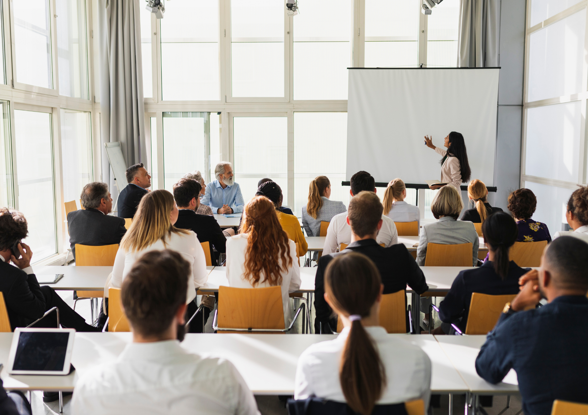 A woman giving a presentation to a diverse group of people in a bright conference room with large windows.