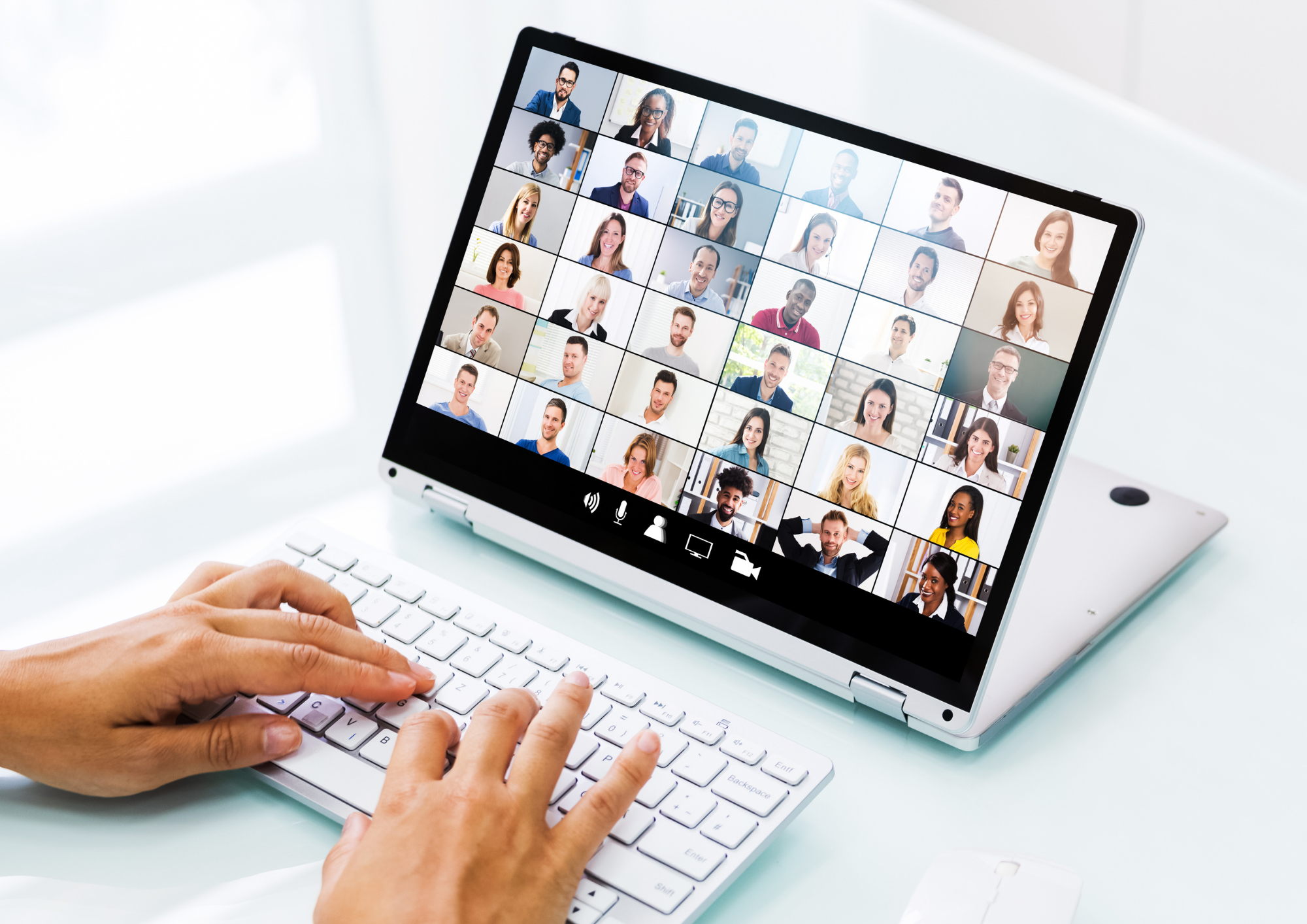 Person using a keyboard on a laptop with a video conference call showing multiple diverse participants on the screen.