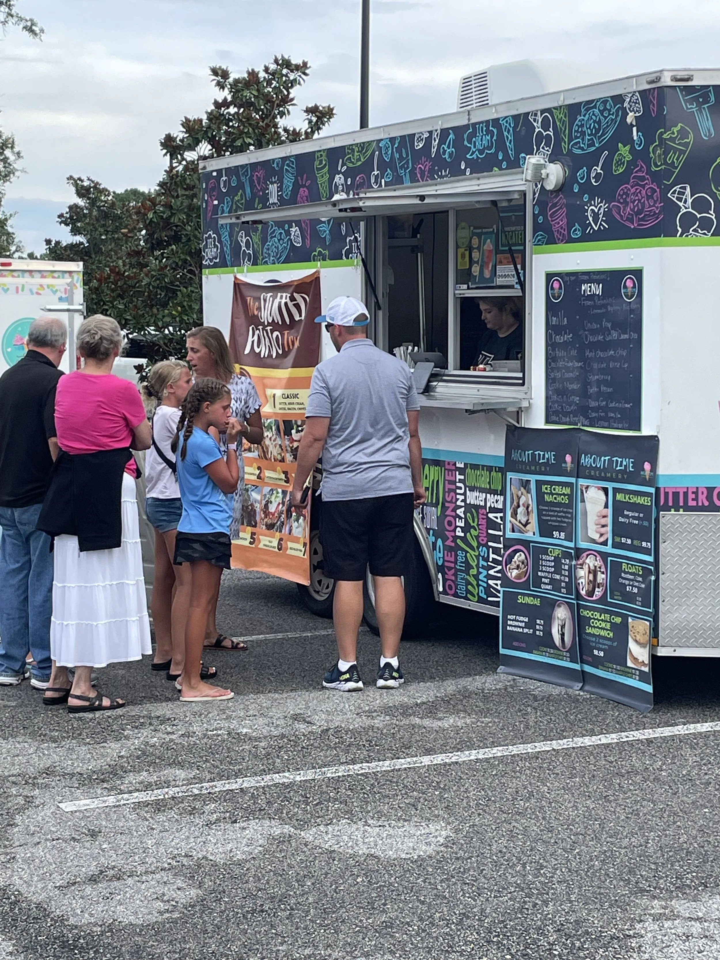 People standing in line at an ice cream truck, with children and adults, on a cloudy day.