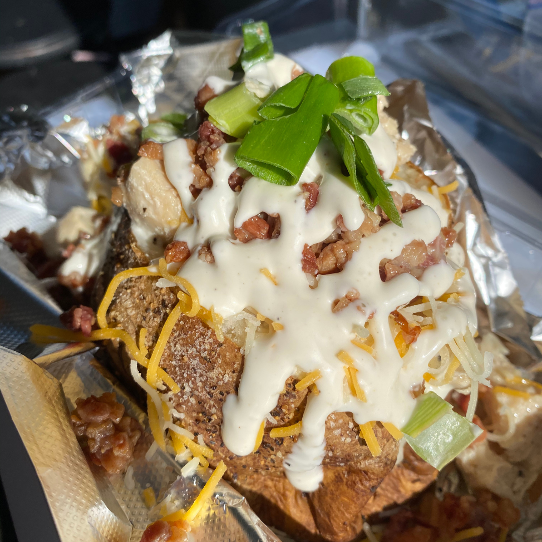 Loaded baked potato topped with shredded cheese, sour cream, bacon bits, and chopped green onions.