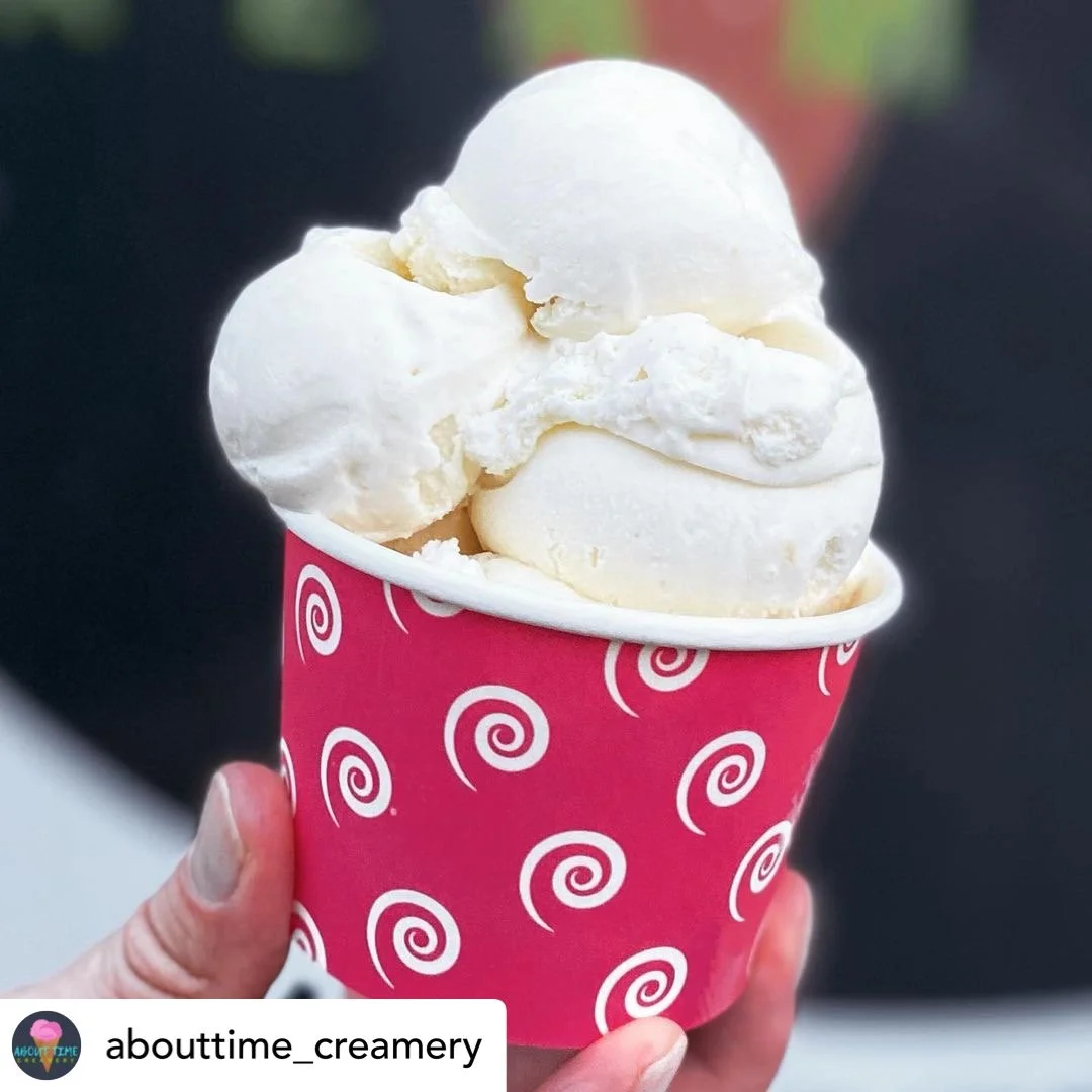 A hand holding a pink cup with white spiral patterns, filled with two scoops of vanilla ice cream.