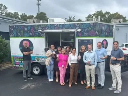 Group of eight people posing in front of a mobile food truck or promotional vehicle in a parking lot.