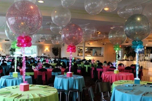 Balloon centerpieces with large transparent balloons and colorful ribbons at a decorated banquet hall for a celebration or event.
