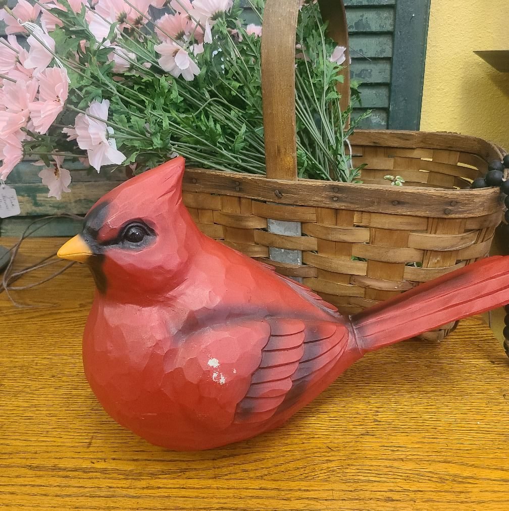 Painted wooden decorative bird resembling a cardinal with a red body, black face, and yellow beak placed on a wooden surface.
